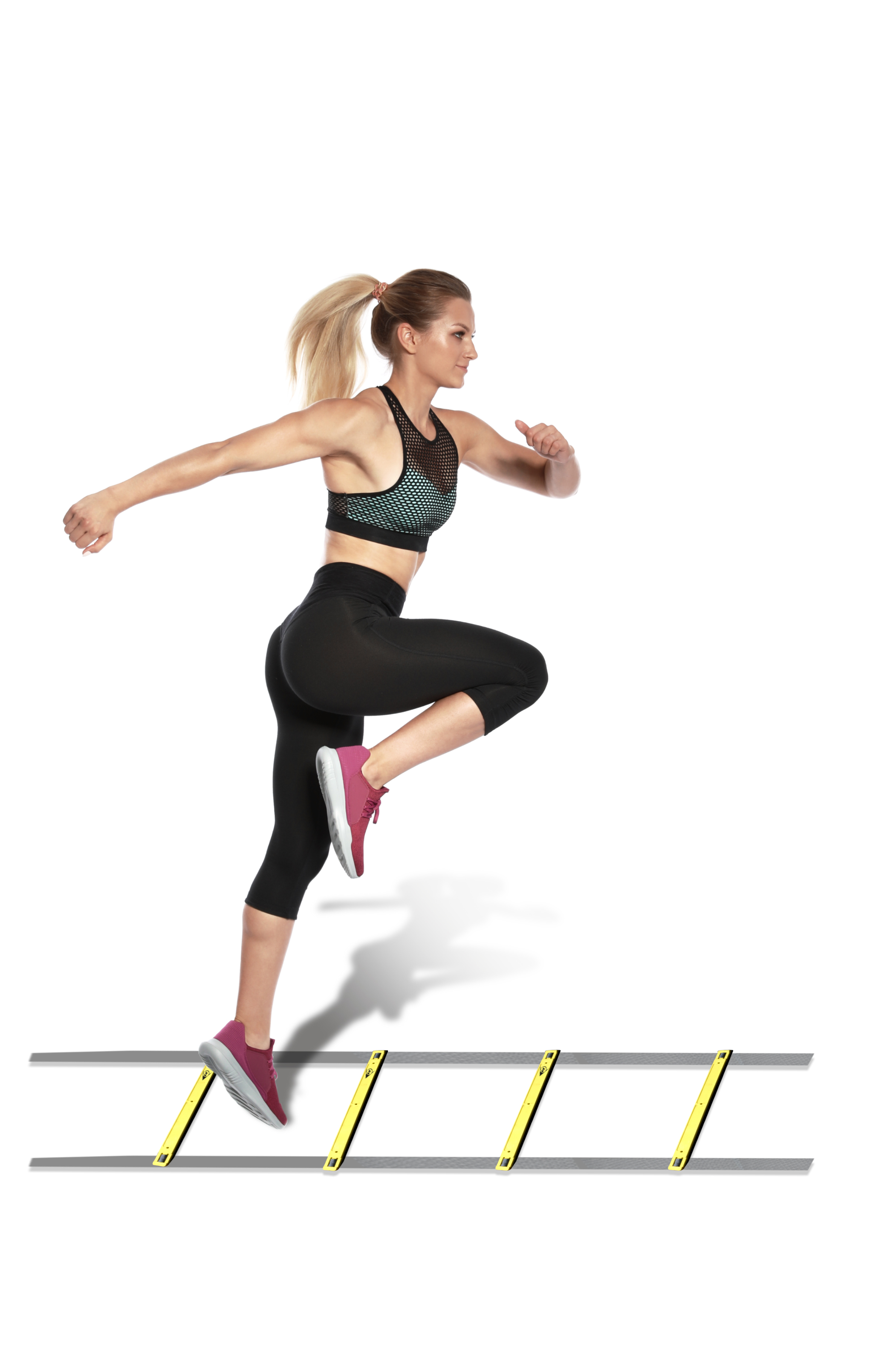 A woman in athletic wear jumps over hurdles. She has blonde hair, and is in mid-air, legs bent. Yellow hurdles are present.
