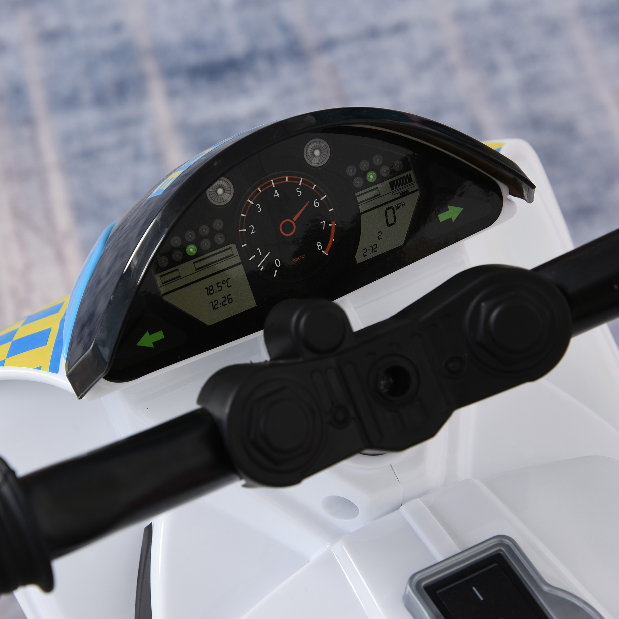 Primo piano del cruscotto di una moto giocattolo con indicatori, tachimetro e display della temperatura. Manubrio nero e carrozzeria bianca visibili.