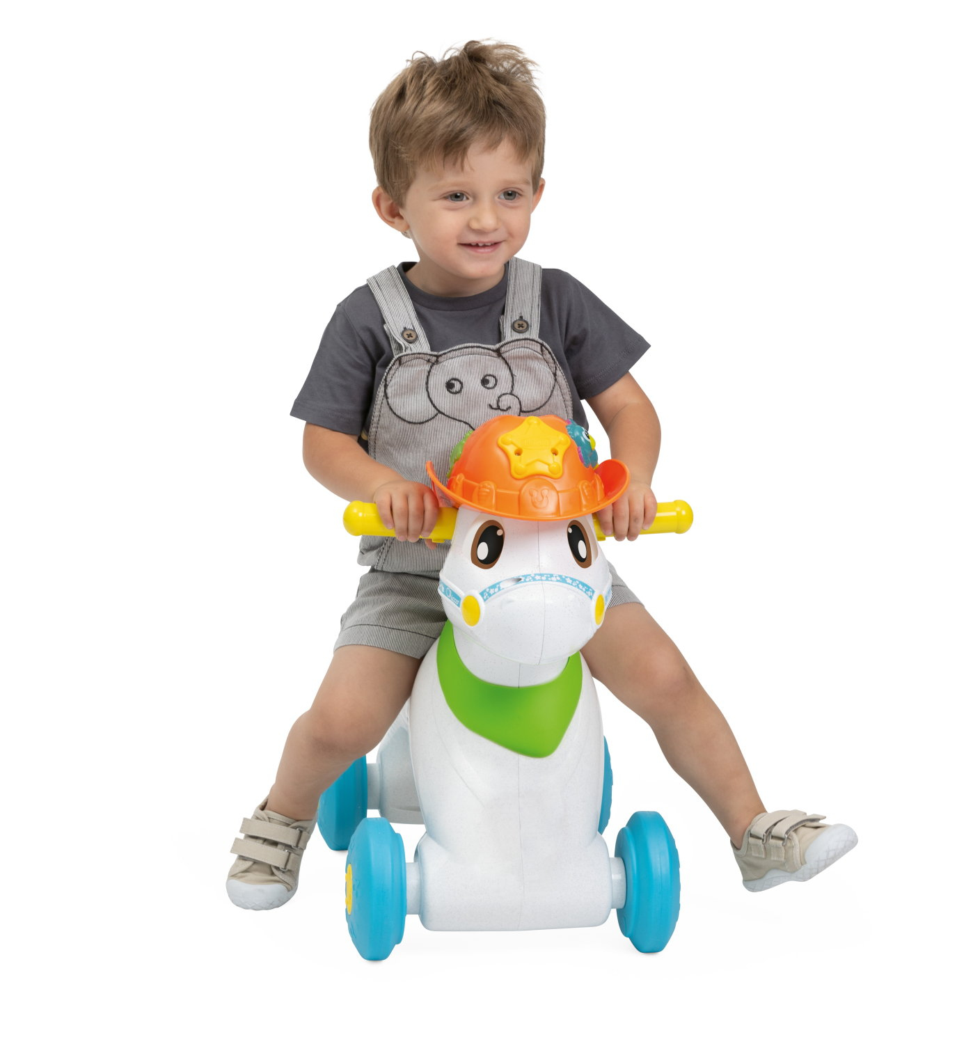 Un bambino cavalca un cavallo giocattolo bianco con ruote blu, con un cappello da cowboy. Sorride, vestito con una tuta grigia e una maglietta.