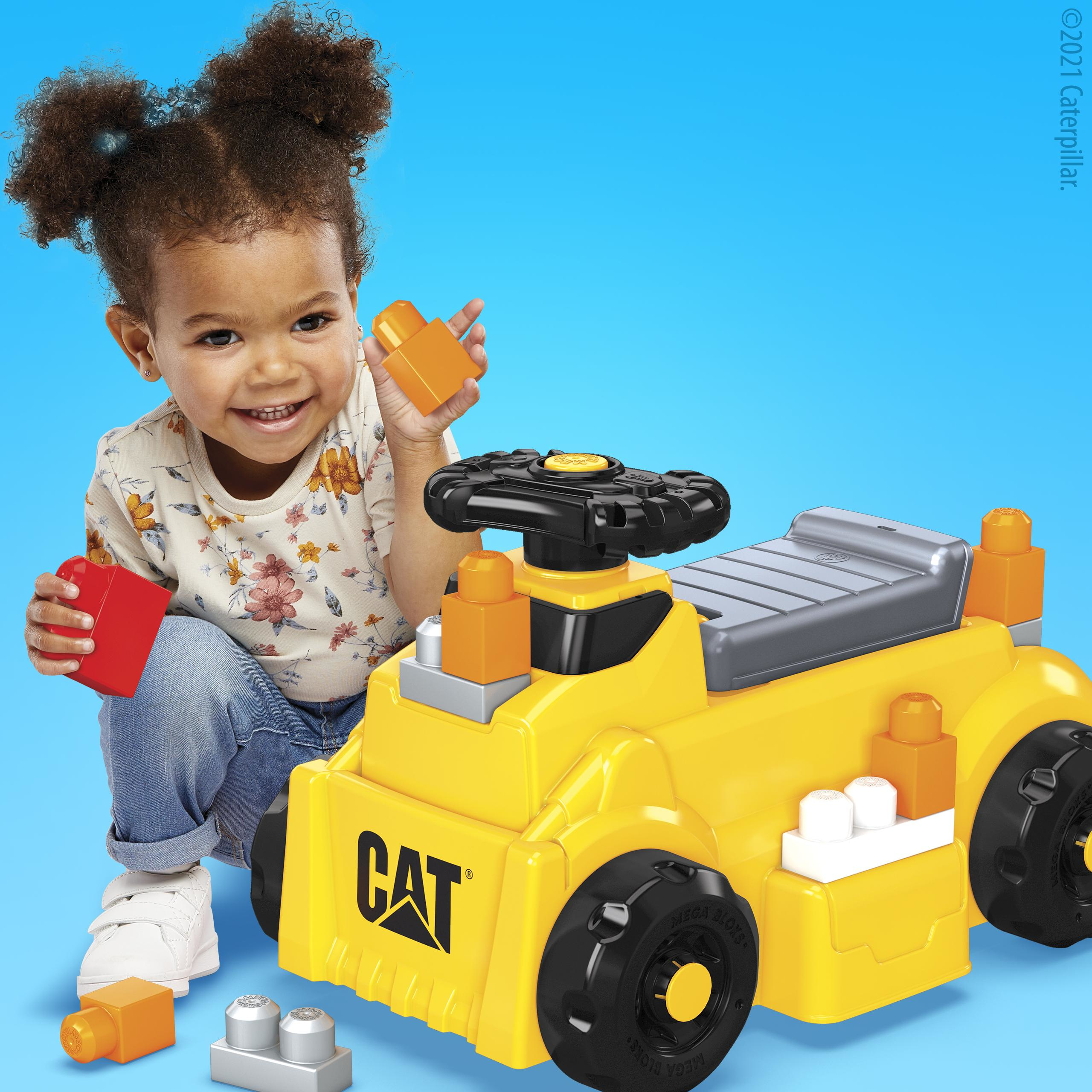 Un bambino sorridente gioca con un camion giocattolo CAT giallo e blocchi colorati. Lo sfondo è azzurro.