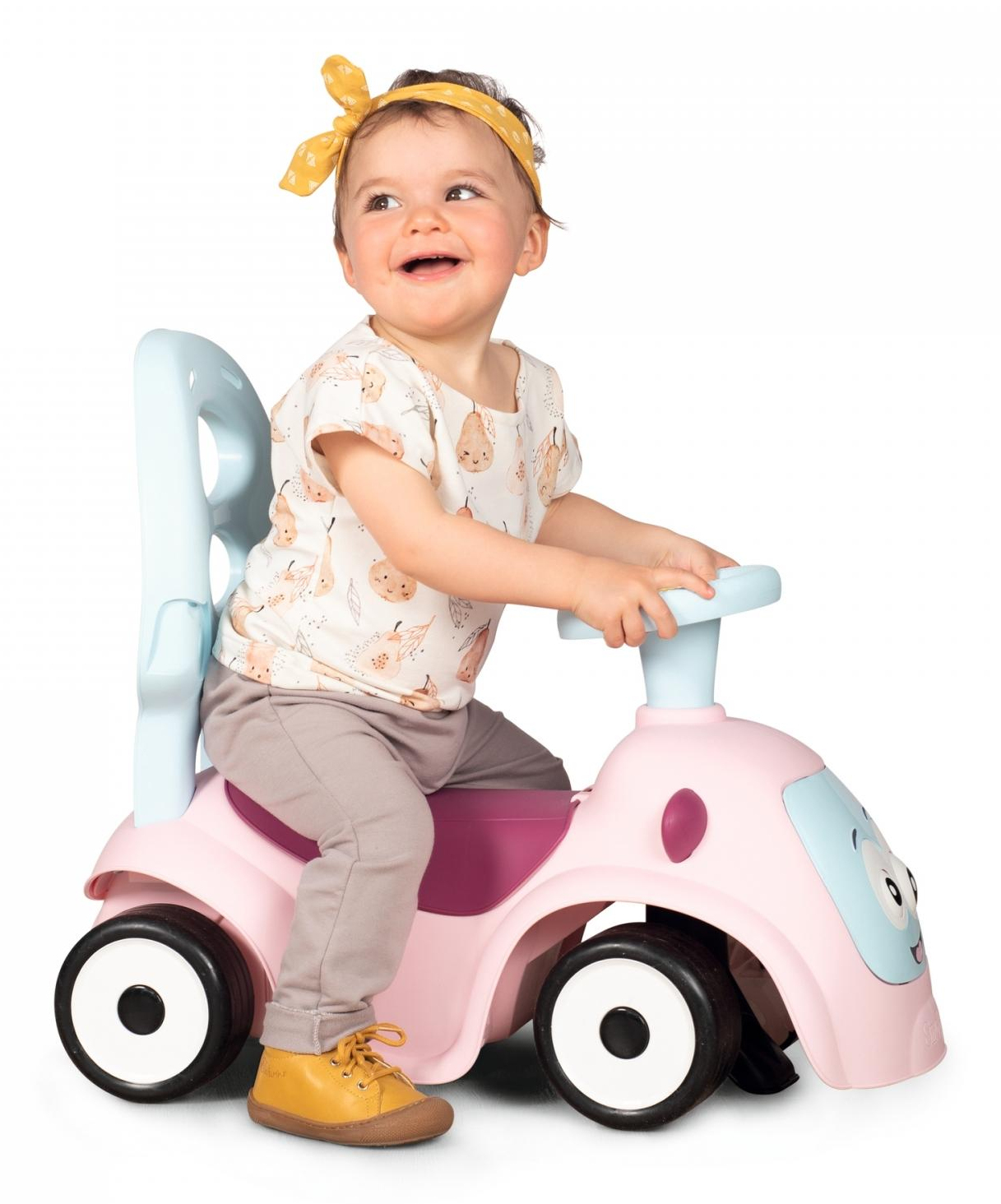 Ein lächelndes Baby sitzt auf einem rosa Spielzeugauto, trägt ein gelbes Stirnband und ein Hemd mit Birnenmotiven. Das Auto hat blaue und violette Akzente.