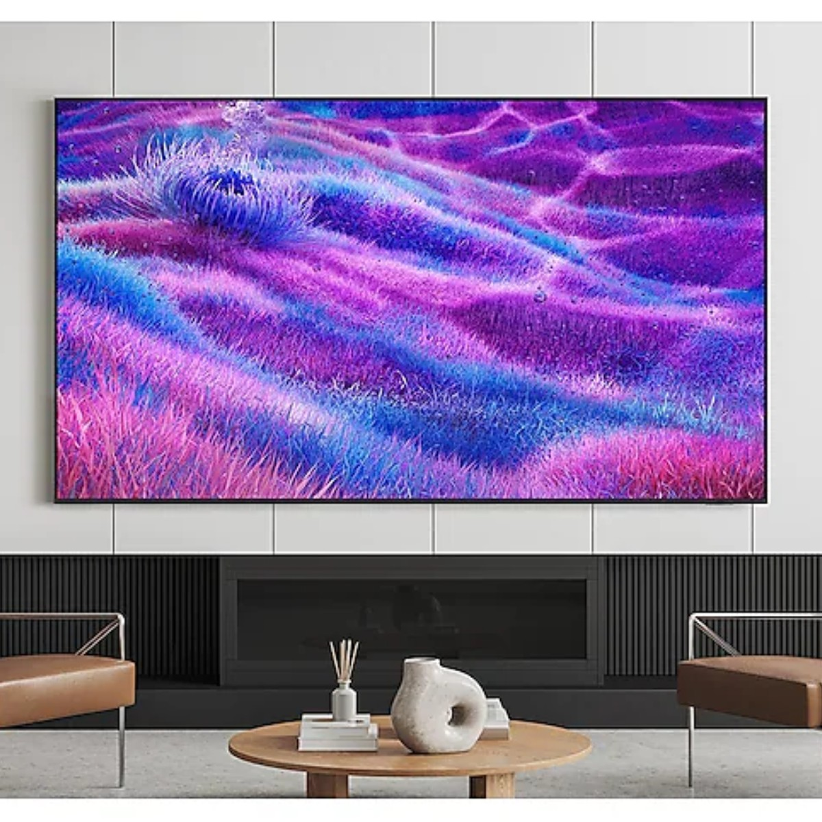 Oprawione dzieło sztuki przedstawia pole fioletowych, niebieskich i różowych form przypominających trawę. Poniżej widoczne są kominek i meble.