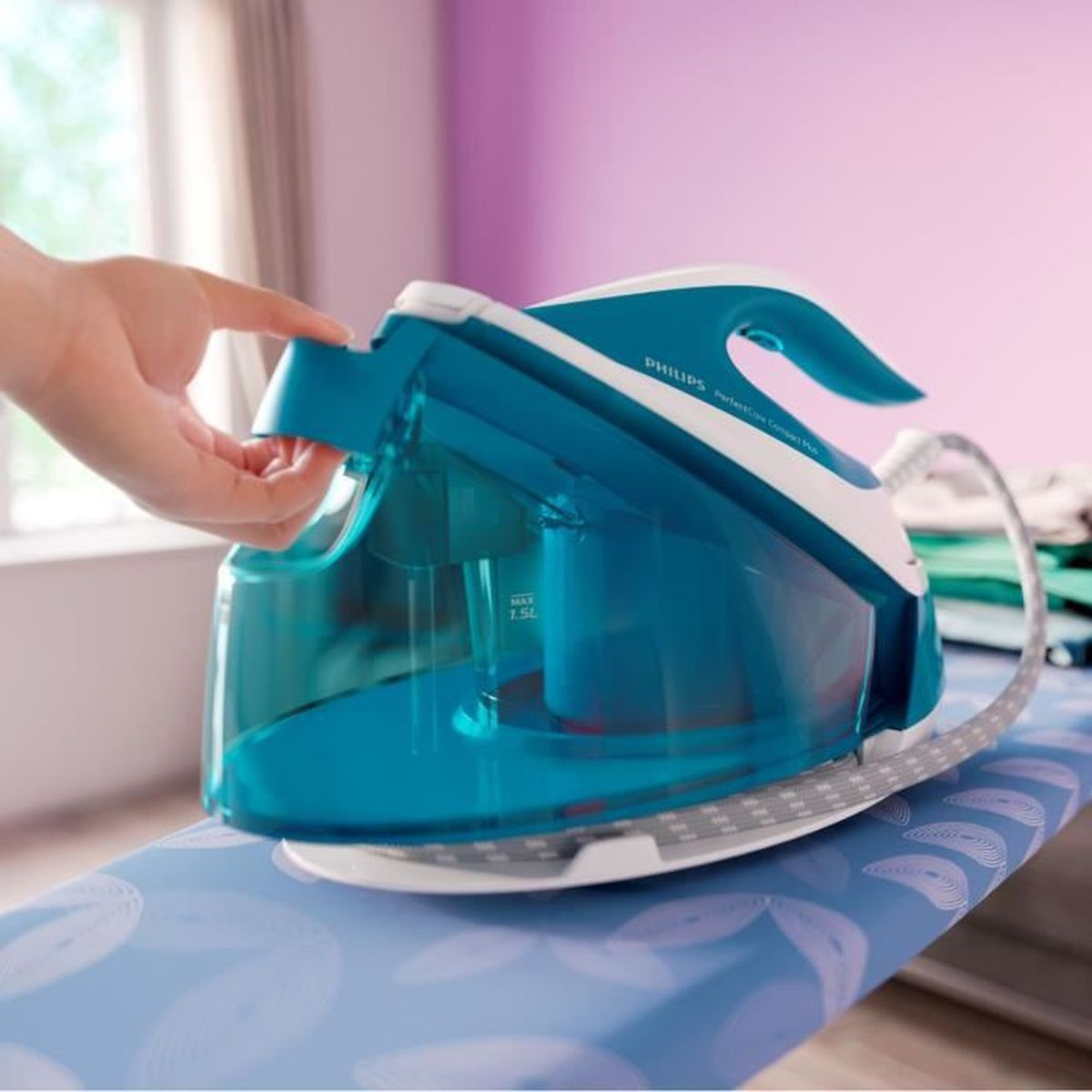 Eine Hand öffnet den blauen Wassertank eines Philips-Bügeleisens. Das Bügeleisen steht auf einem Bügelbrett mit blauem Blumenmuster.