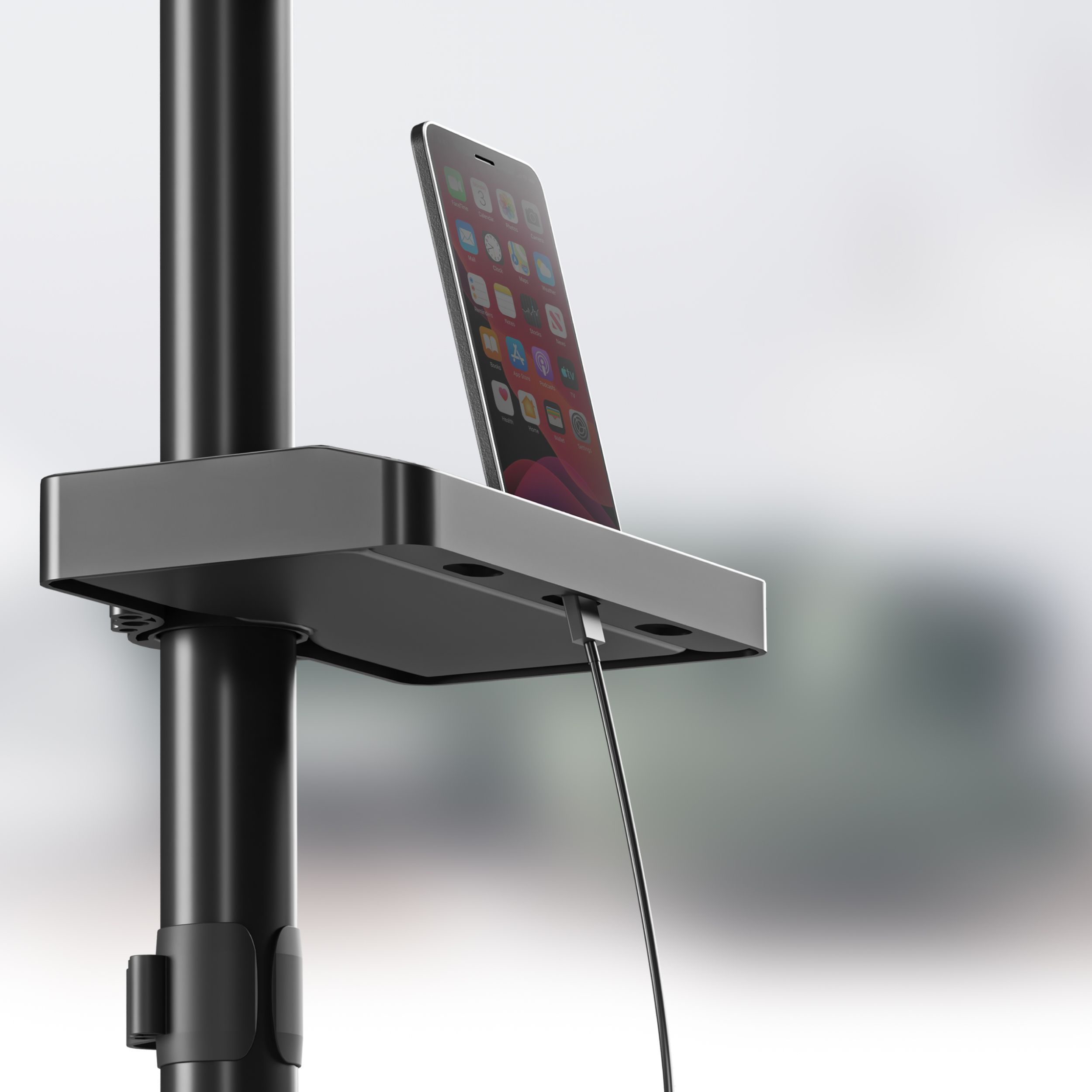Un supporto per telefono nero tiene uno smartphone. Un cavo di ricarica è collegato. Lo sfondo è un ambiente ufficio sfocato.