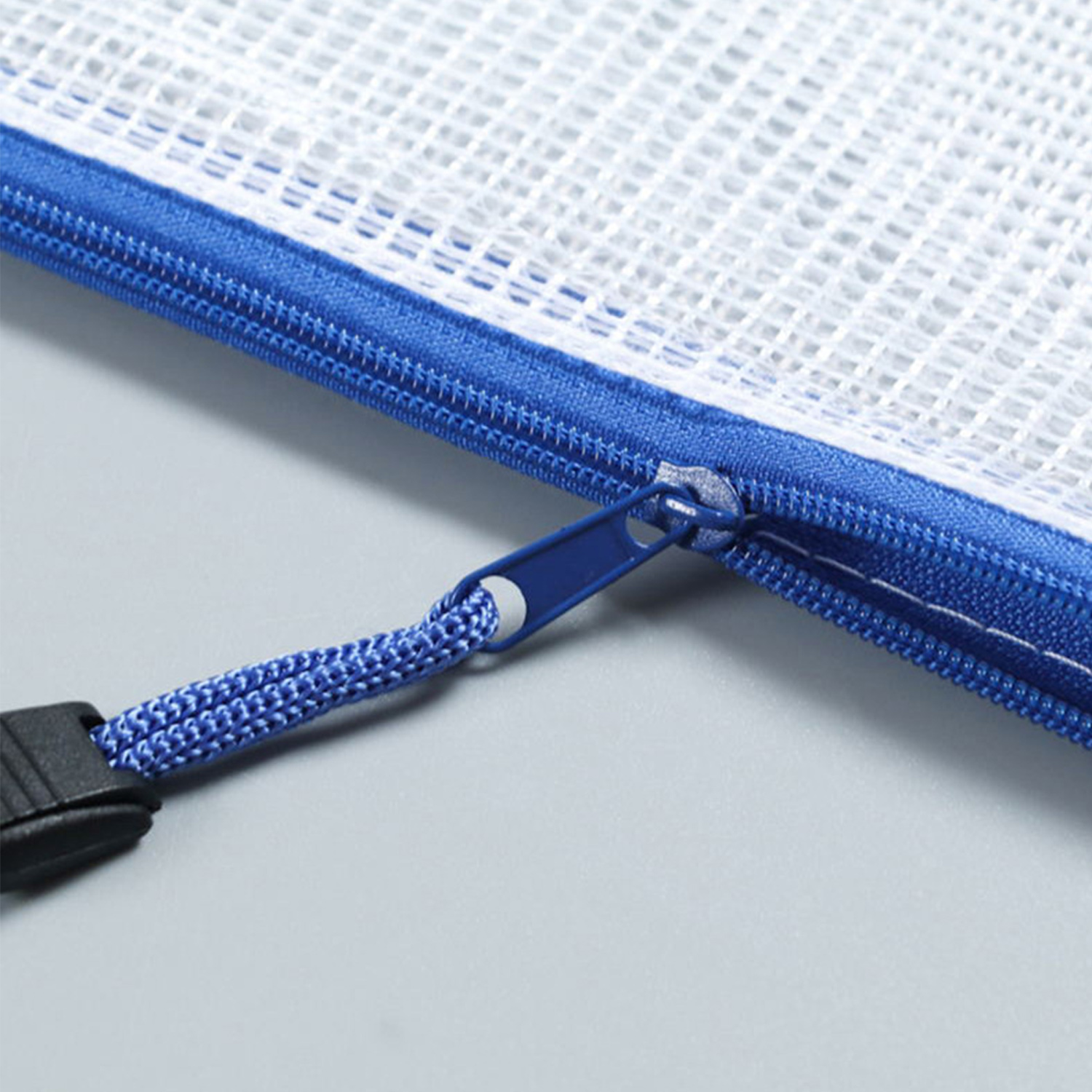 Zbliżenie białej siatkowej torby z niebieskim zamkiem błyskawicznym i uchwytem. Dołączony jest niebieski sznurek i czarna klamra.