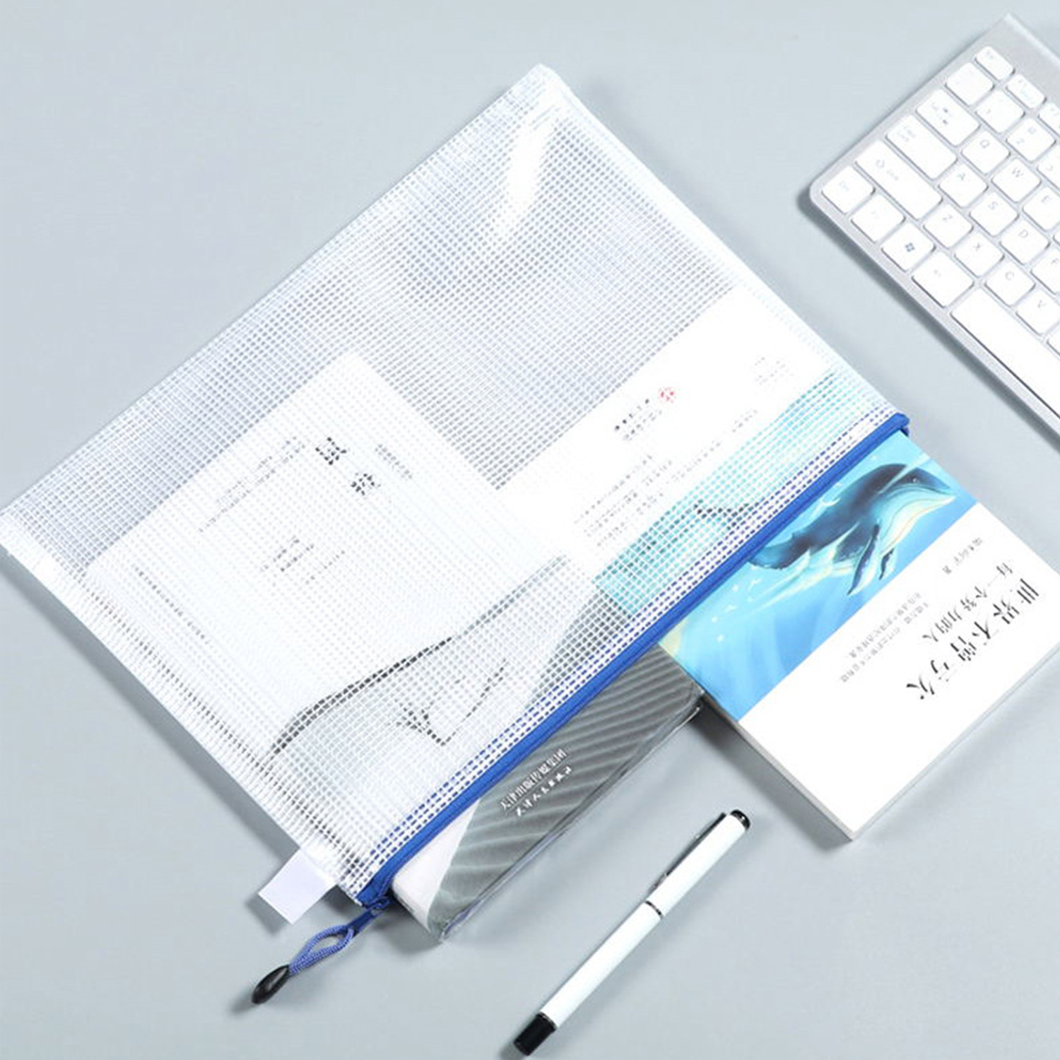 Biała torba na dokumenty z siatki z dokumentami, książką, długopisem i klawiaturą na szarej powierzchni.