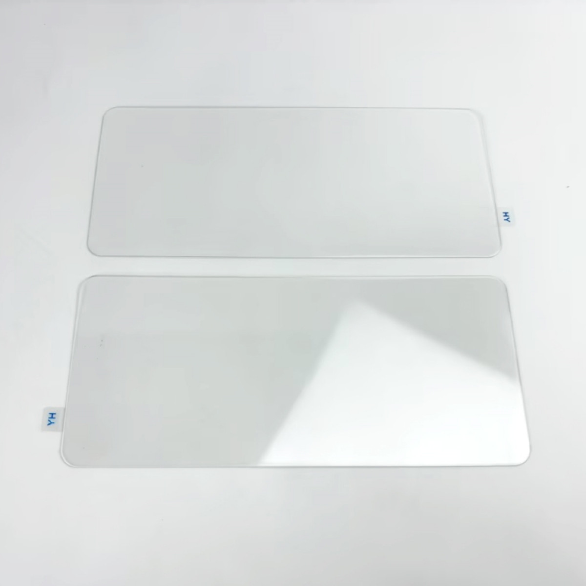 Due pezzi rettangolari di vetro trasparente su una superficie bianca, ciascuno con una piccola etichetta blu. Uno ha "HV", l'altro "YH".