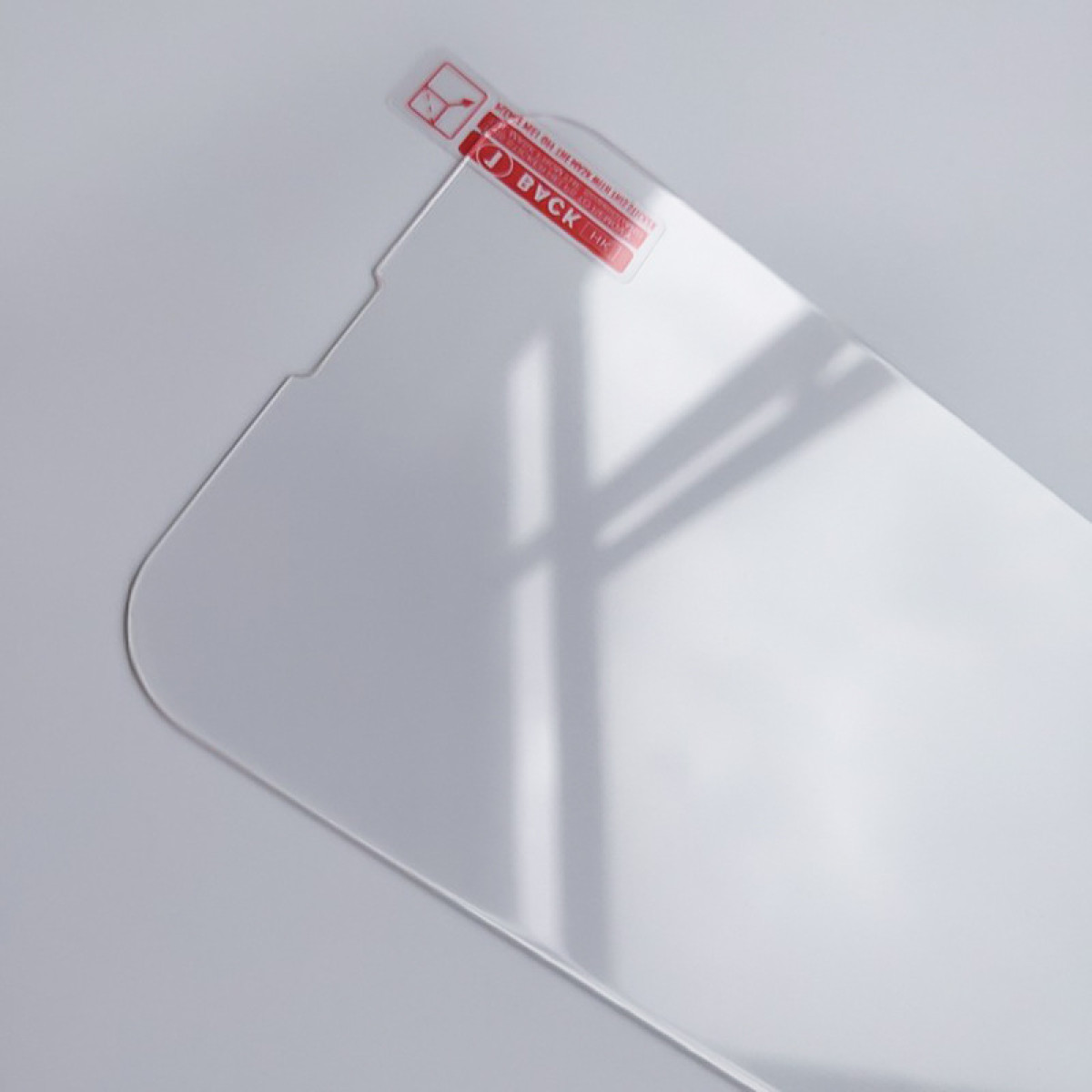 Een heldere schermbeschermer met een rood label. De beschermer ligt op een wit oppervlak en werpt een schaduw.