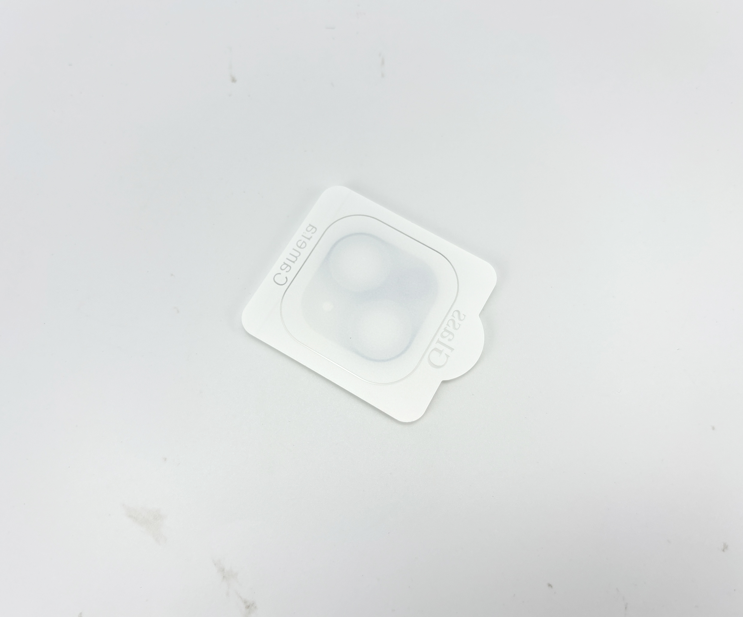 Een witte plastic cameralensbeschermer op een wit oppervlak. Het heeft drie ronde lensafdekkingen. Tekst erop.