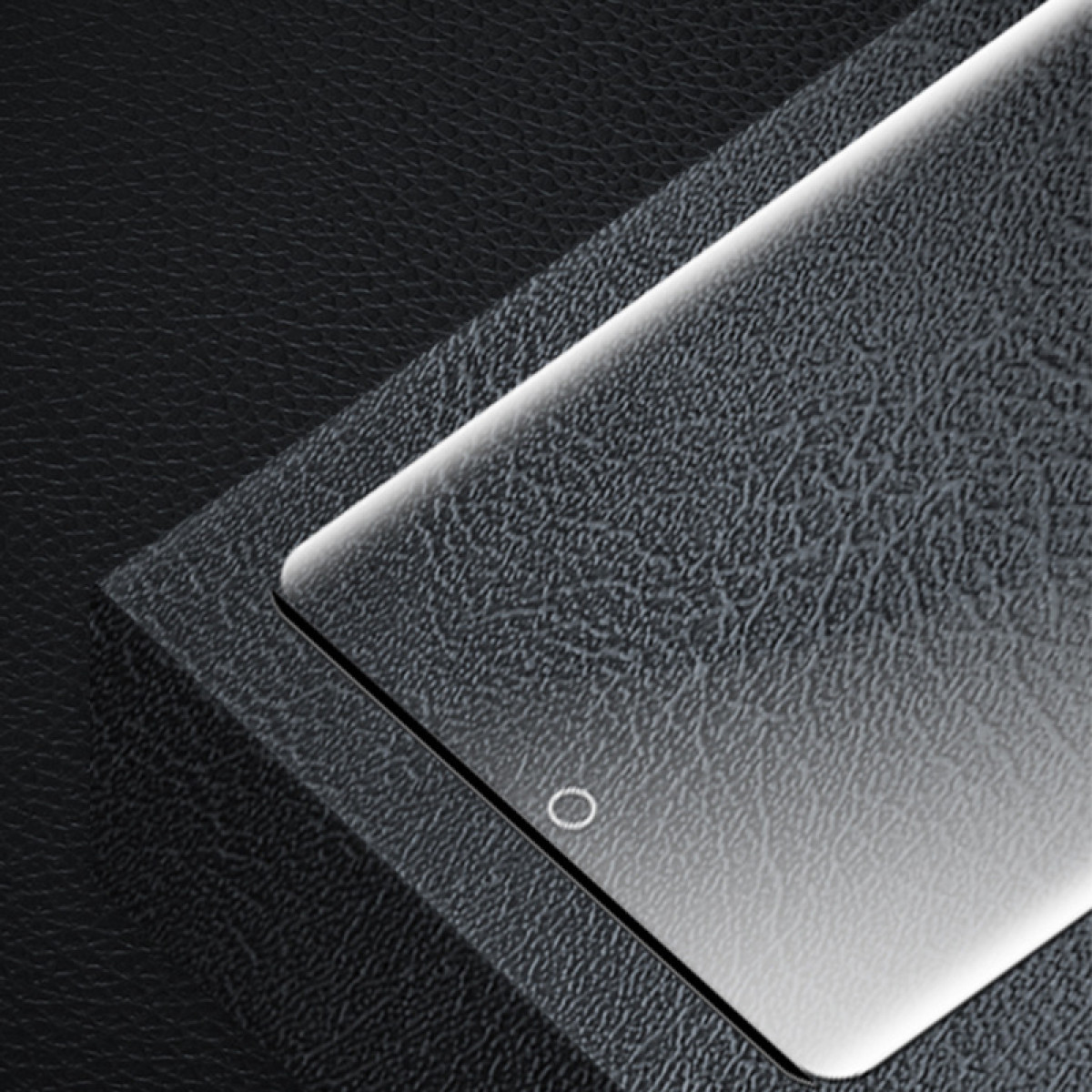 Ochraniacz ekranu smartfona na teksturowanej ciemnej powierzchni. Małe kółko widoczne na dole ochraniacza.