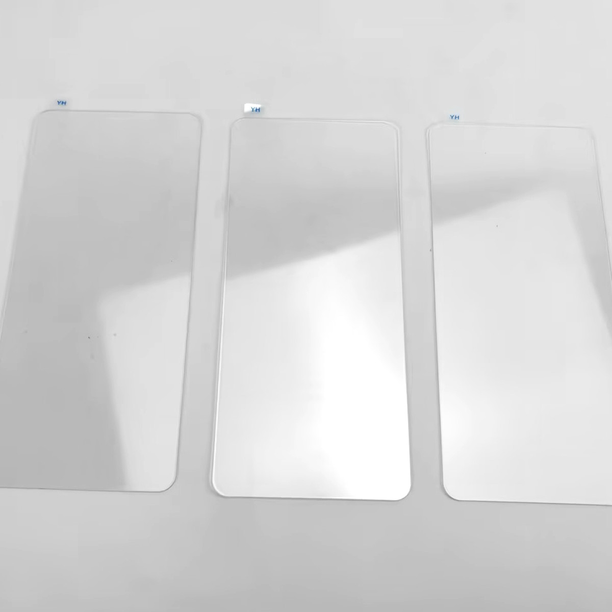 Trzy prostokątne, przezroczyste ochraniacze ekranu ułożone pionowo na białej powierzchni. Każdy ma etykietę 'YH'.