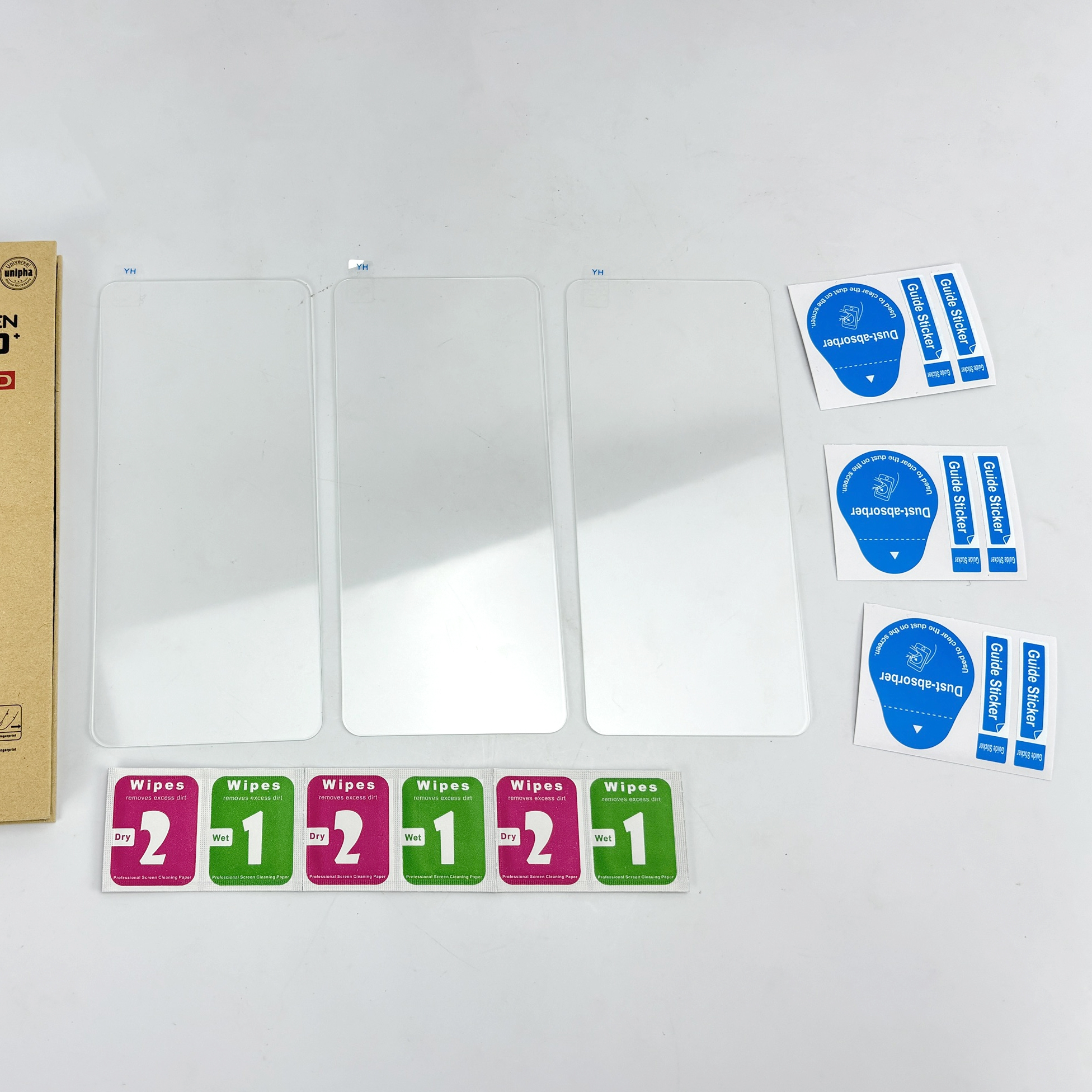 Obraz przedstawia ochraniacze ekranu, chusteczki czyszczące i naklejki prowadzące na białej powierzchni. Opakowanie widoczne po lewej.