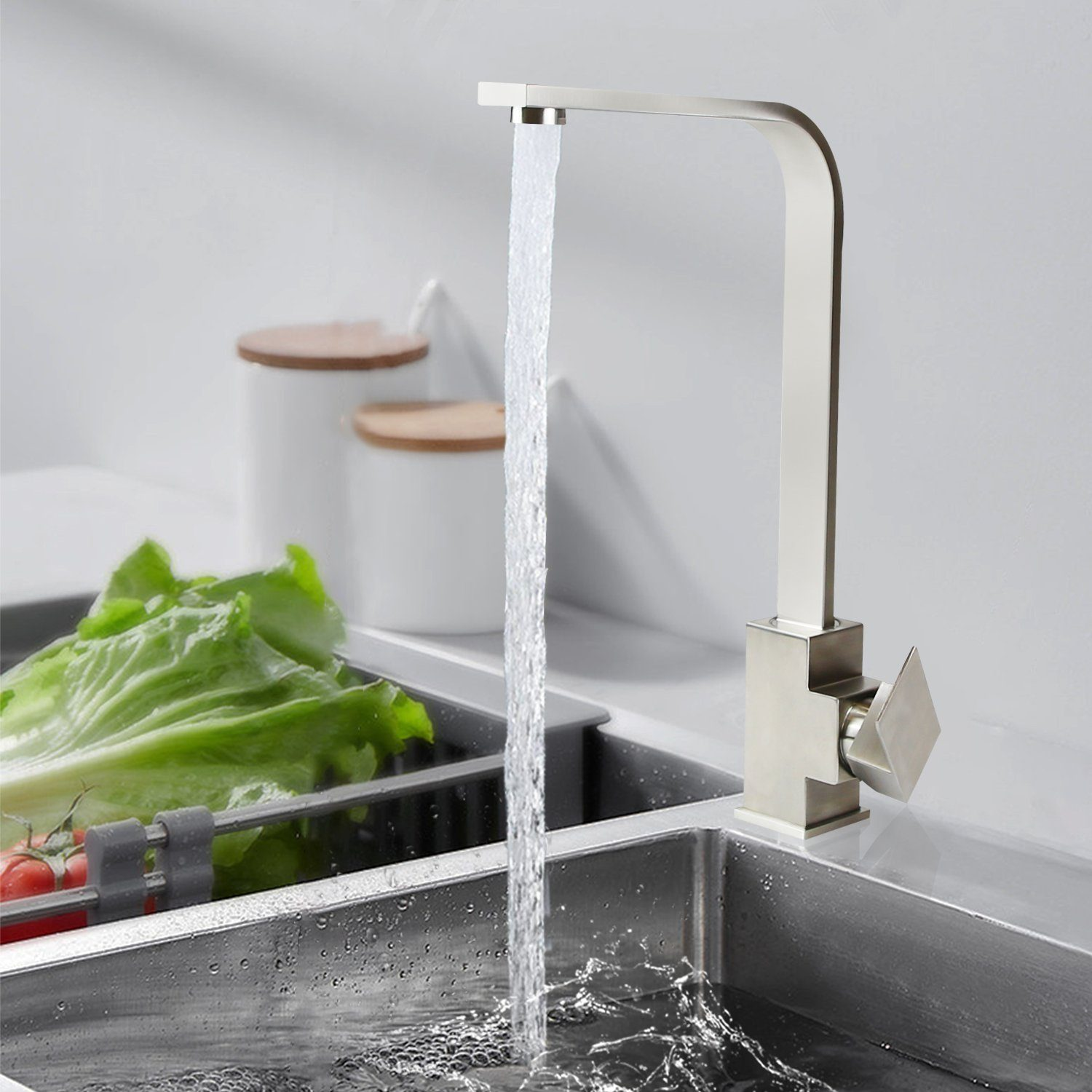 Stalowa bateria zlewozmywakowa wlewa wodę do zlewu kuchennego. Warzywa, w tym sałata i pomidory, znajdują się w zlewie. Białe słoiki w tle.