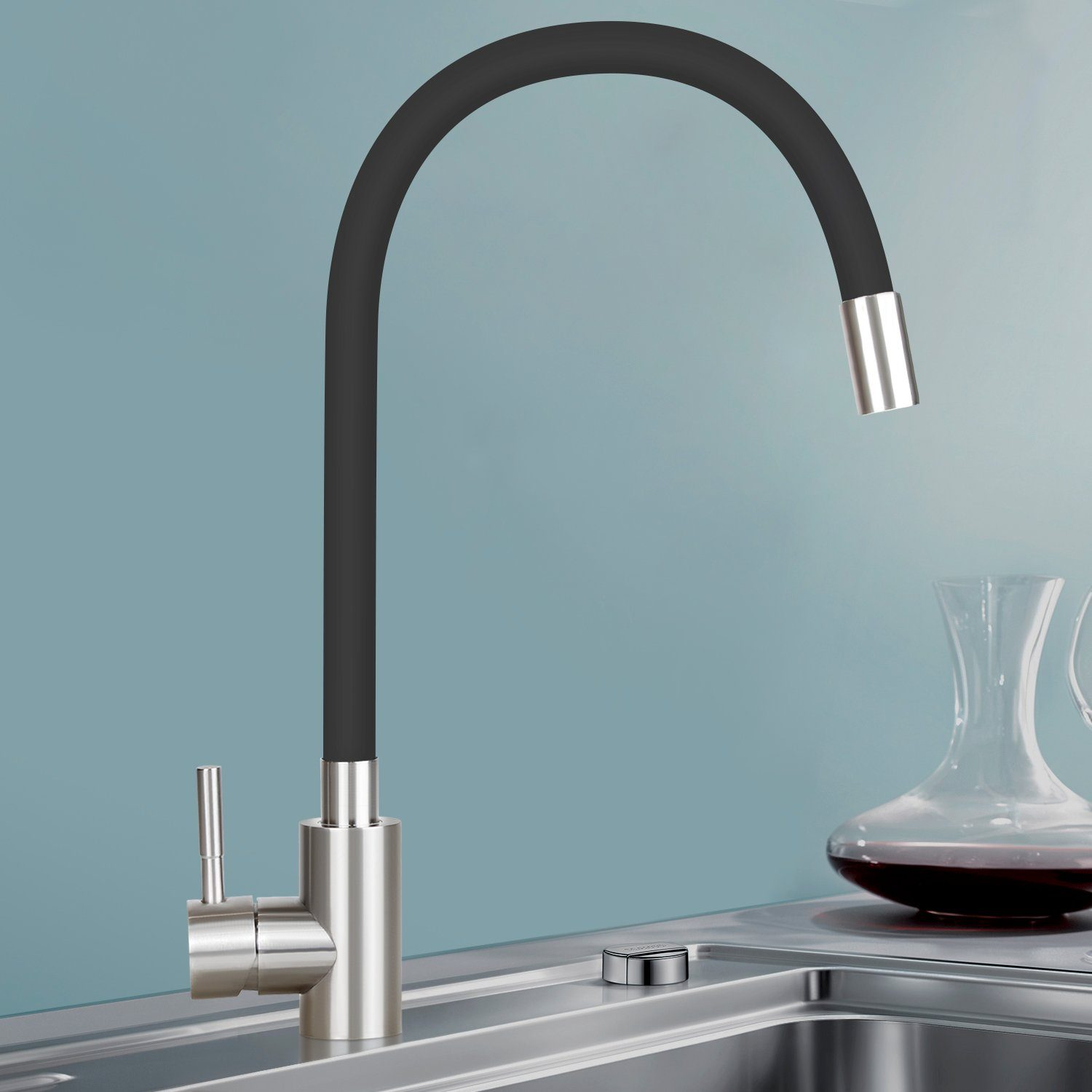 Nowoczesna bateria kuchenna z czarną, elastyczną wylewką. Karafka z czerwoną cieczą stoi obok zlewu. Niebieskie tło.