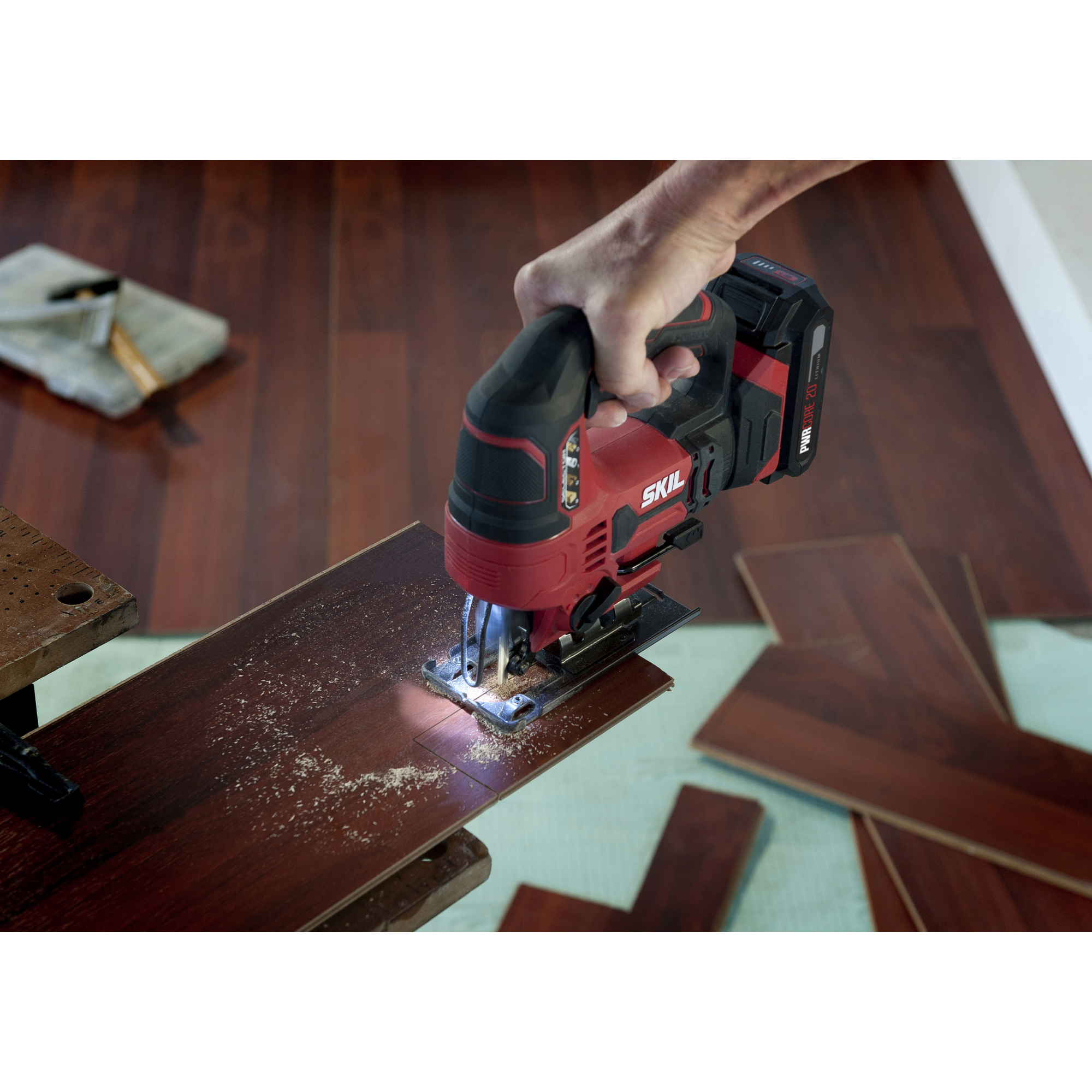 Een hand gebruikt een rode en zwarte Skil decoupeerzaag om een houten plank te zagen. Zaagsel en gezaagde planken zichtbaar.