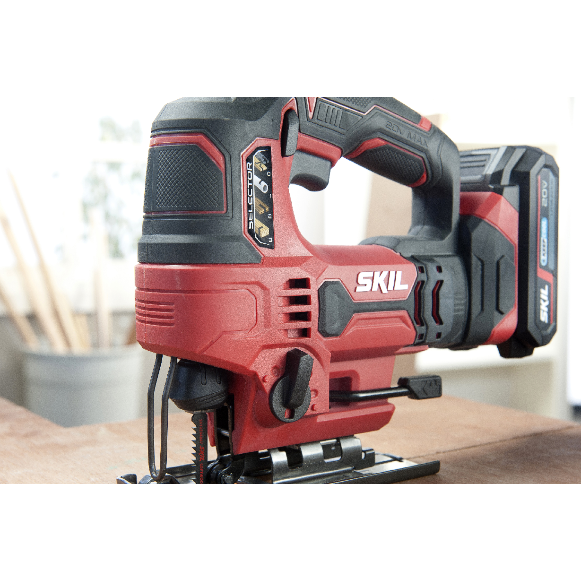 Een rode en zwarte Skil decoupeerzaag op een houten oppervlak. De tool is snoerloos en heeft een batterij. Achtergrond is wazig.
