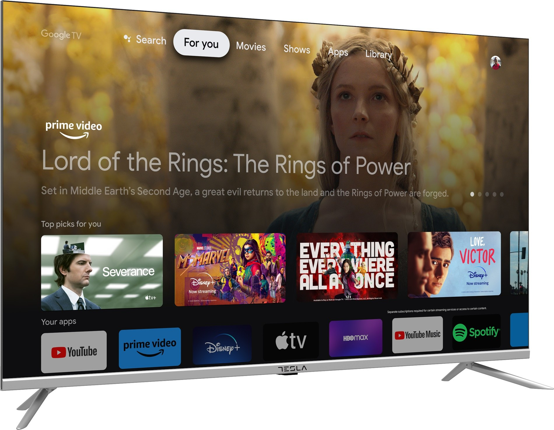 Telewizor Tesla wyświetla interfejs Google TV. Ekran pokazuje 'Władcę Pierścieni' i ikony aplikacji, takie jak Prime Video, Disney+ i YouTube.