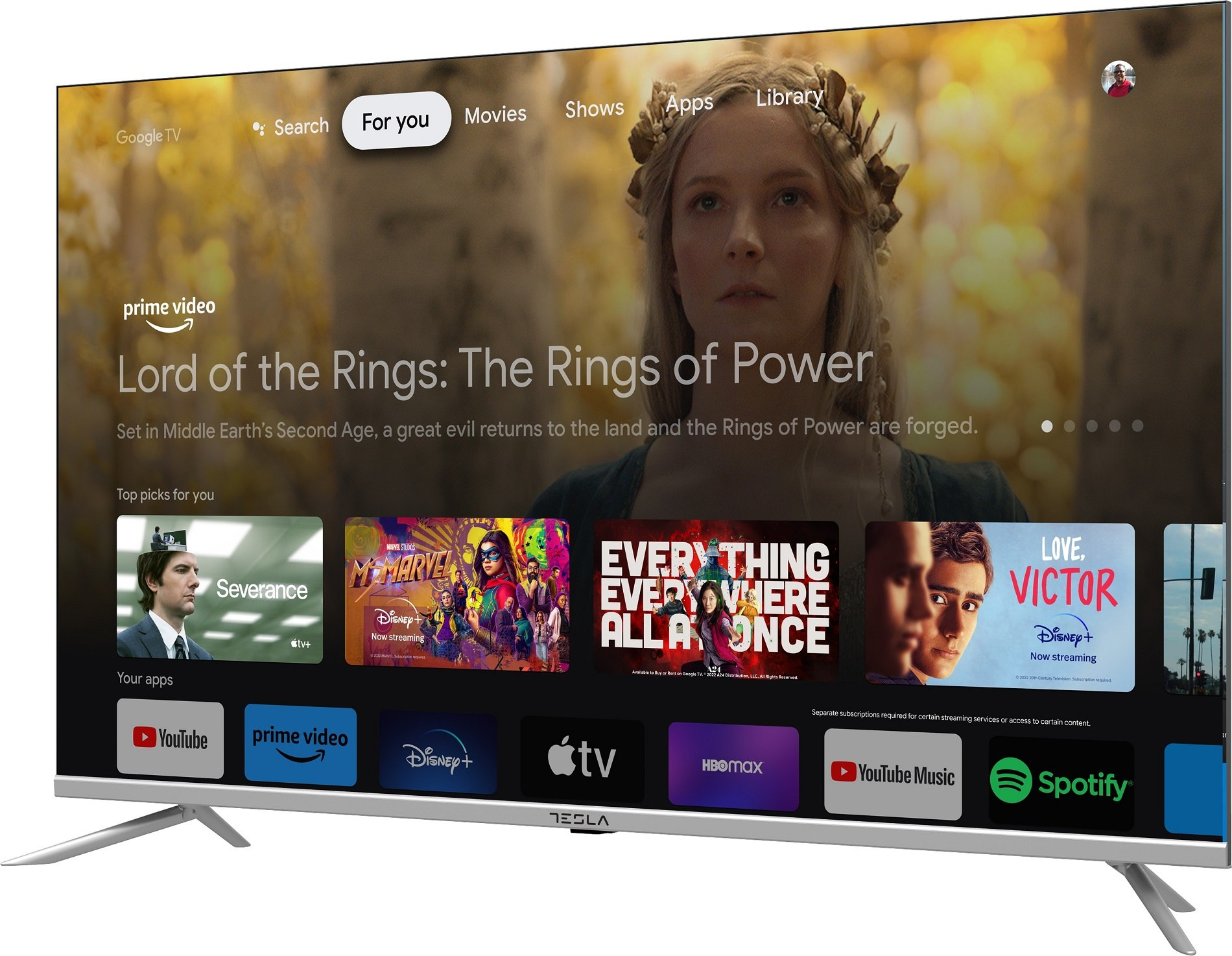 Telewizor Tesla wyświetla interfejs Google TV. Pokazuje treści z 'Władcy Pierścieni'. Widoczne są aplikacje takie jak Prime Video, Disney+ i YouTube.