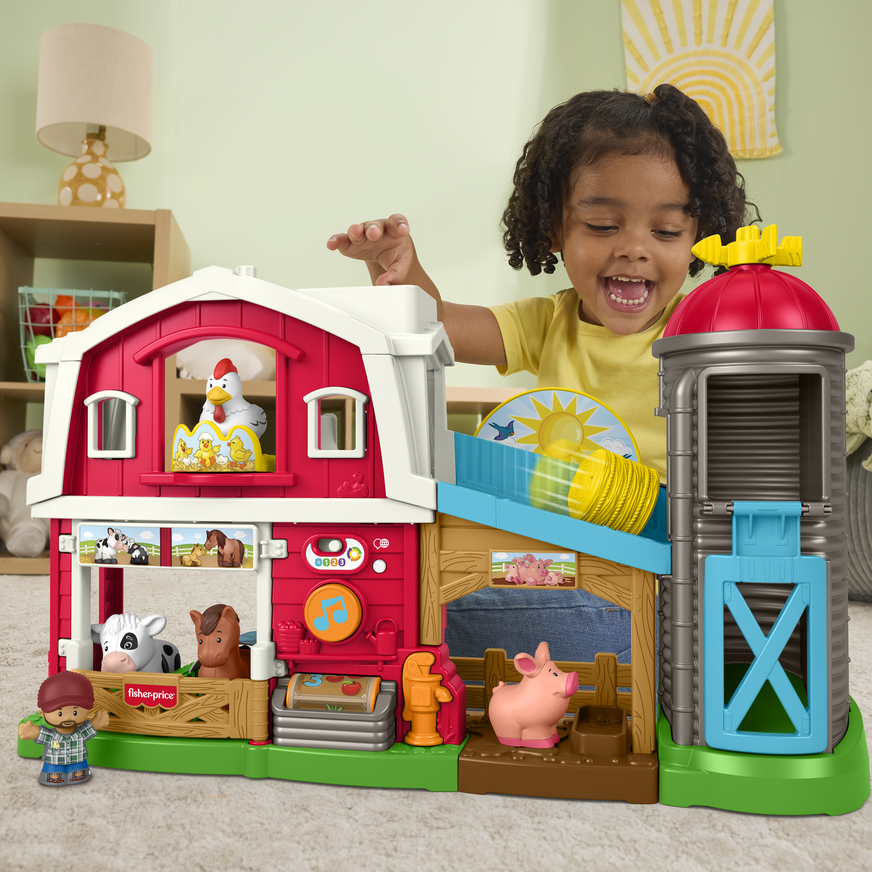 Dziecko bawi się czerwoną i białą farmą. Farma ma zwierzęta, silo i zjeżdżalnię. Dziecko się uśmiecha.