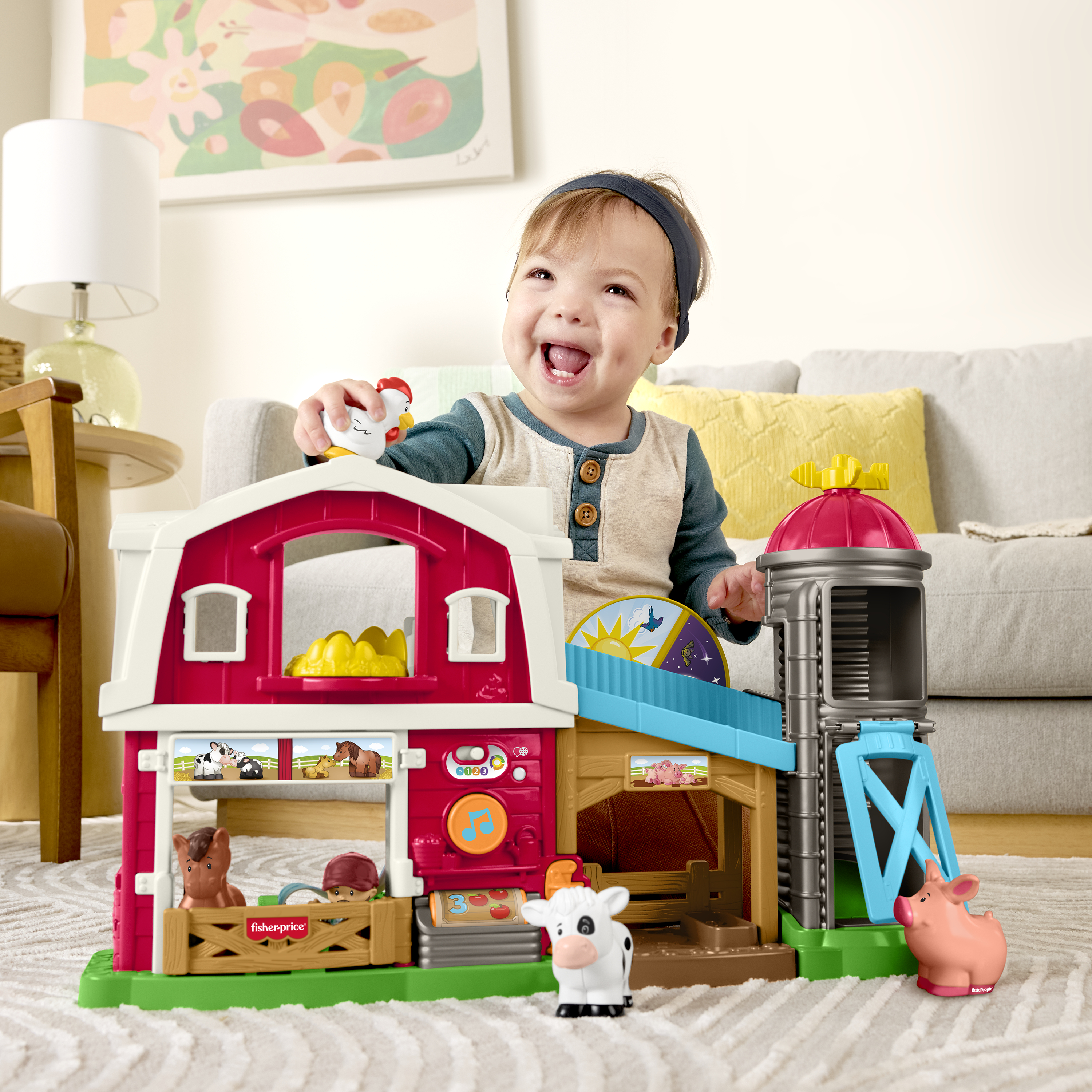 Dziecko uśmiecha się, bawiąc się zabawką gospodarstwem. Zestaw zawiera czerwoną stodołę, zwierzęta i silos.