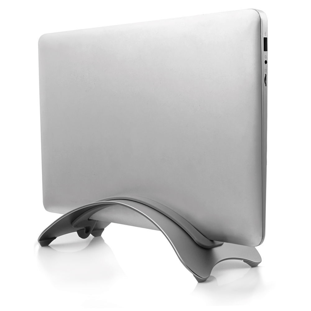 Srebrny laptop w srebrnym stojaku, odbijający się na białej powierzchni. Laptop jest zamknięty.