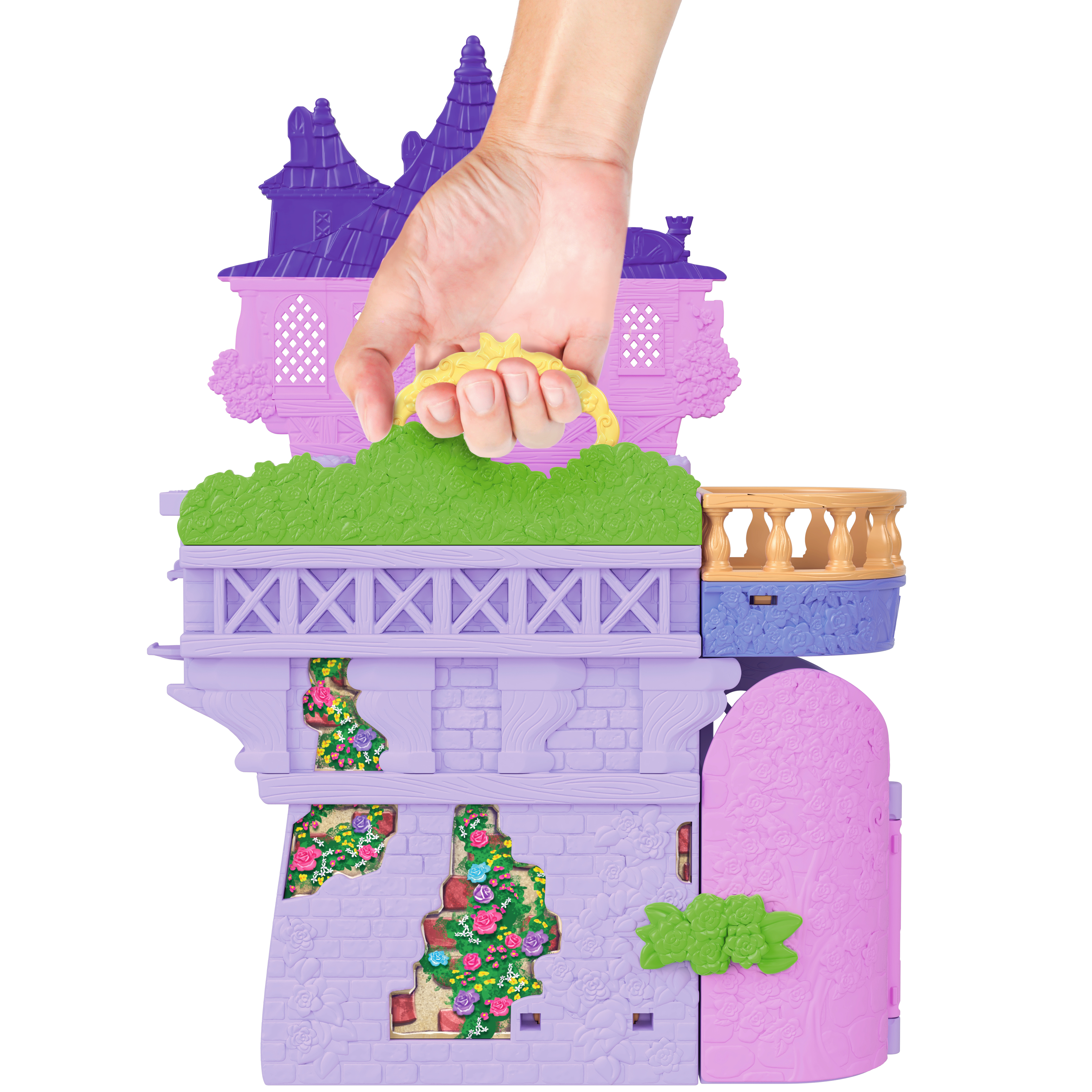Una mano sostiene un castillo de juguete colorido. El castillo tiene paredes moradas y rosas, setos verdes y un asa amarilla.