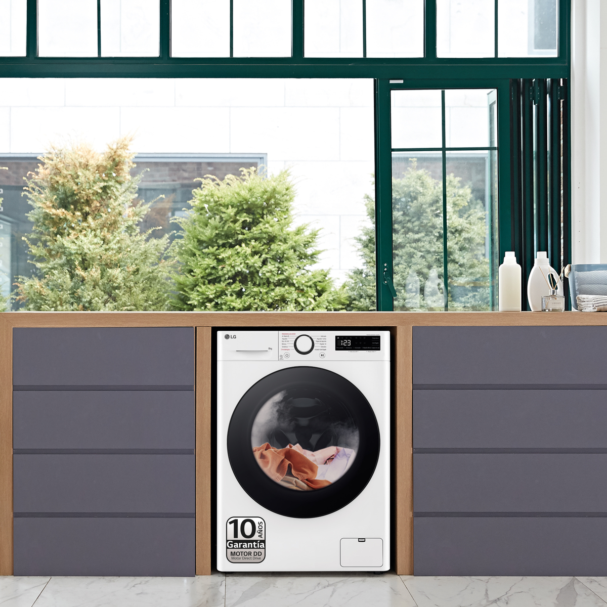 Biała pralka z czarnymi drzwiami i oknem z drzewami na zewnątrz. Szafki są po lewej i prawej stronie.