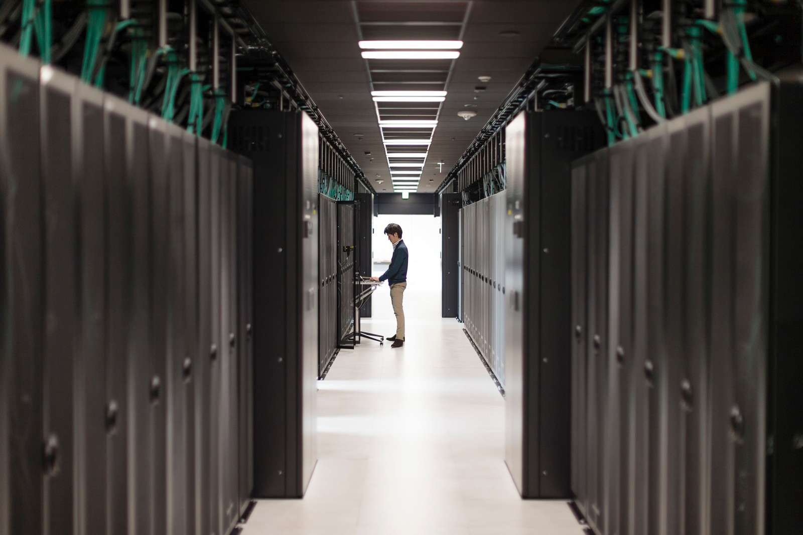 Un uomo in un data center lavora a un computer tra file di server. La stanza è ben illuminata.