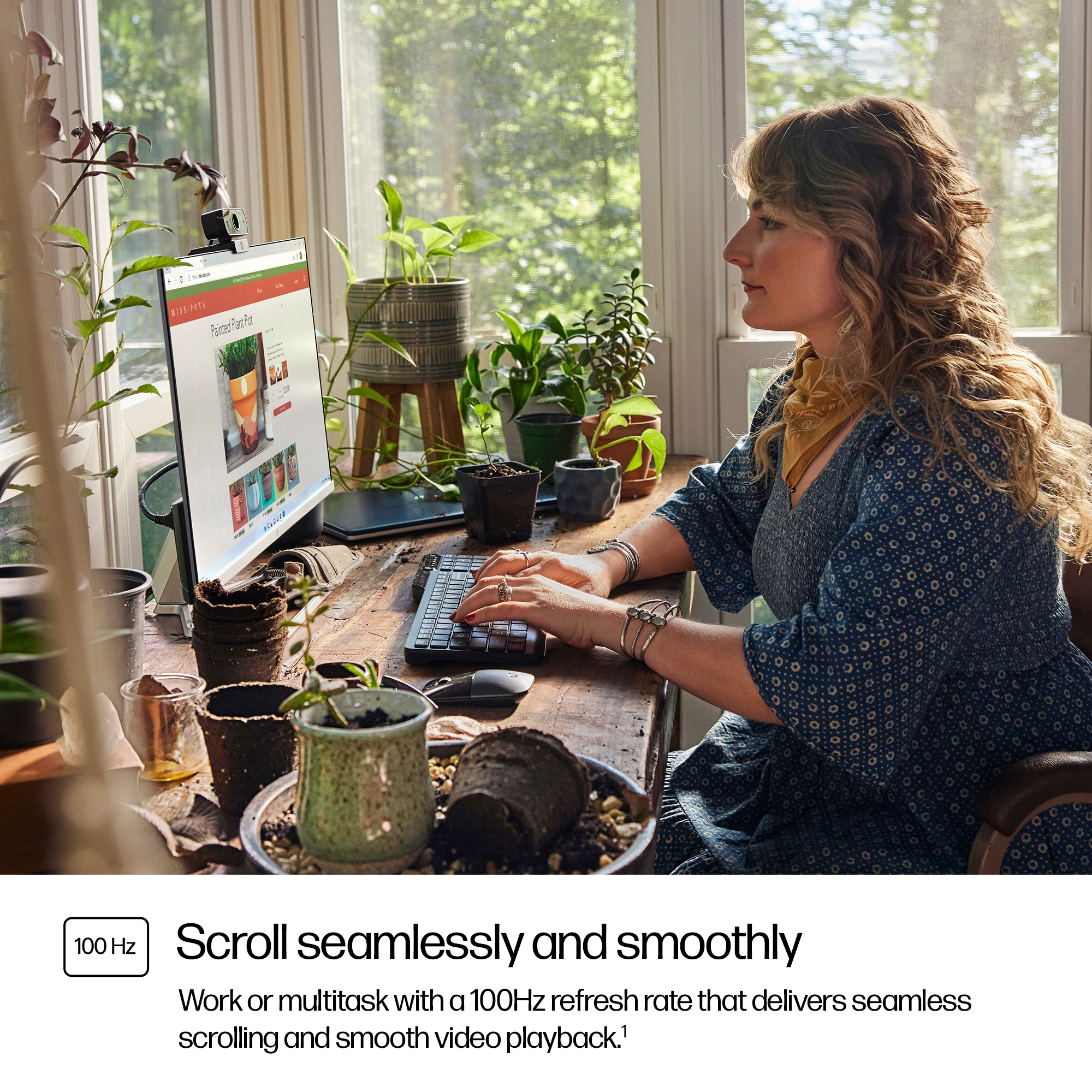 Una donna lavora a una scrivania con computer, tastiera e mouse. La circondano delle piante. Lo schermo mostra un sito web sui vasi dipinti.