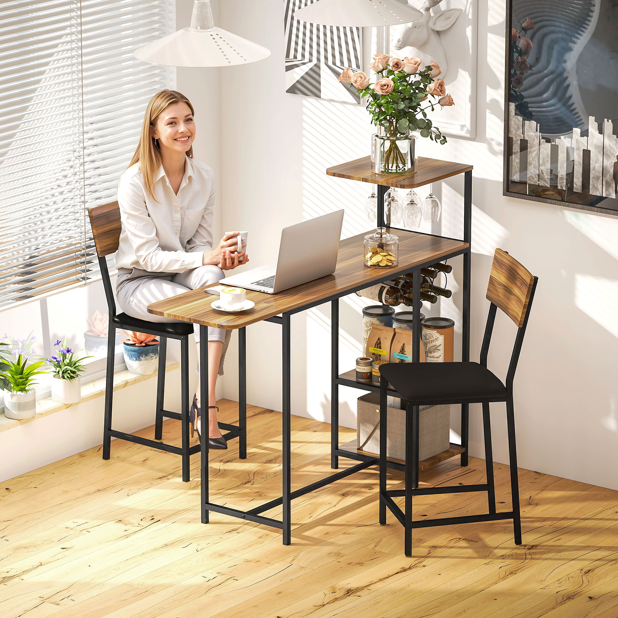 Una mujer está sentada en una mesa de bar con una computadora portátil y café. Hay taburetes de bar, copas de vino y flores. La habitación tiene luz natural.