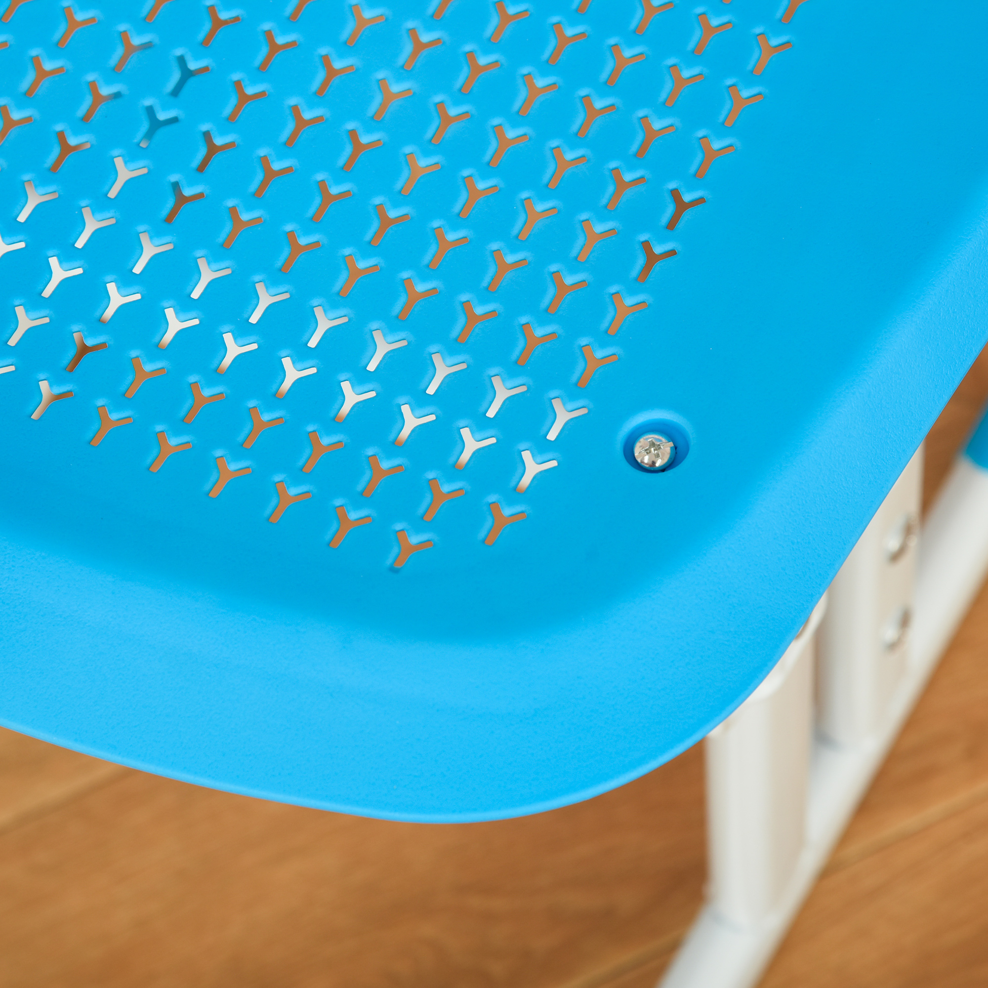 Primo piano di una seduta di sedia in plastica blu con ritagli a forma di Y. È visibile una vite. Lo sfondo mostra pavimento in legno e gambe della sedia bianche.