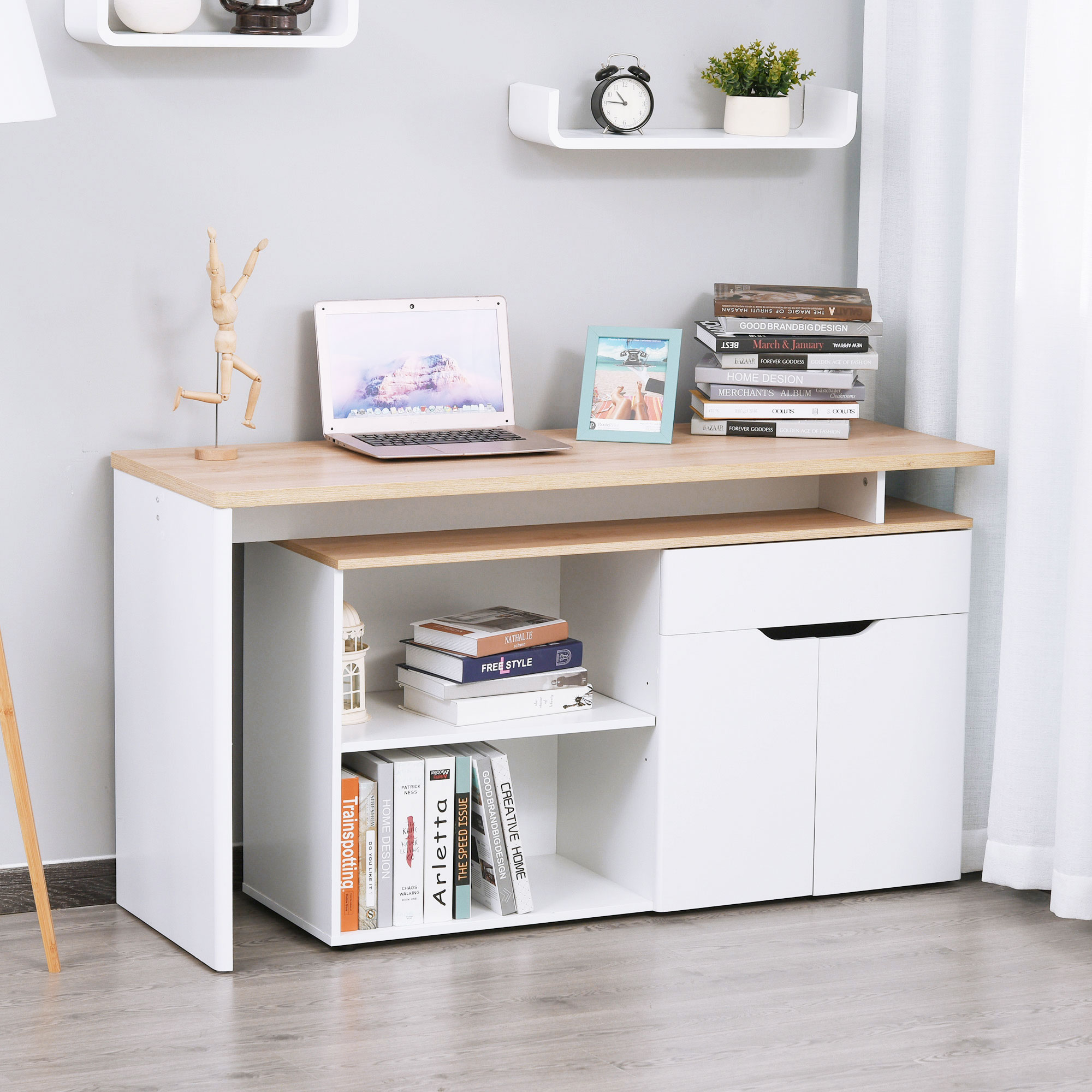Una scrivania bianca con un laptop, libri e una figura di legno. Un piccolo orologio e una pianta sono su uno scaffale sopra.