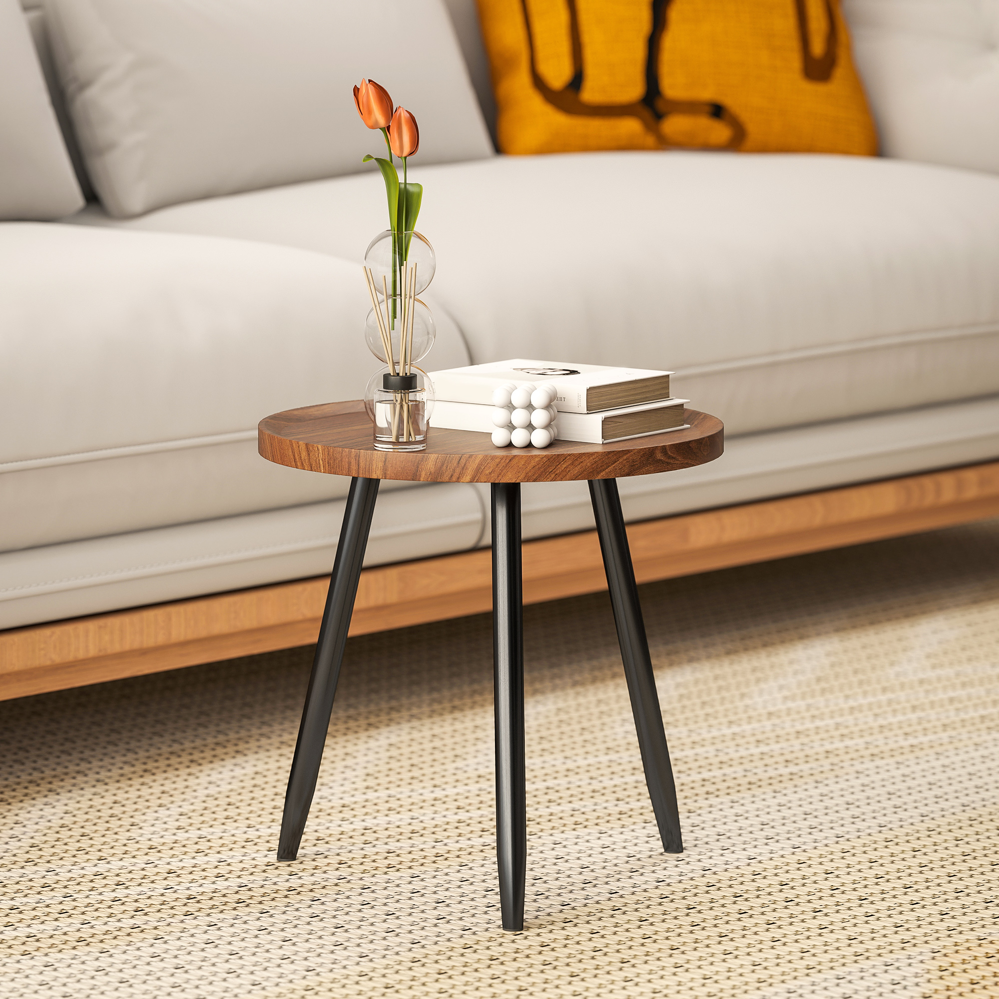 Un tavolino rotondo in legno con gambe nere. Sopra ci sono libri, palline decorative e un vaso con tulipani arancioni.