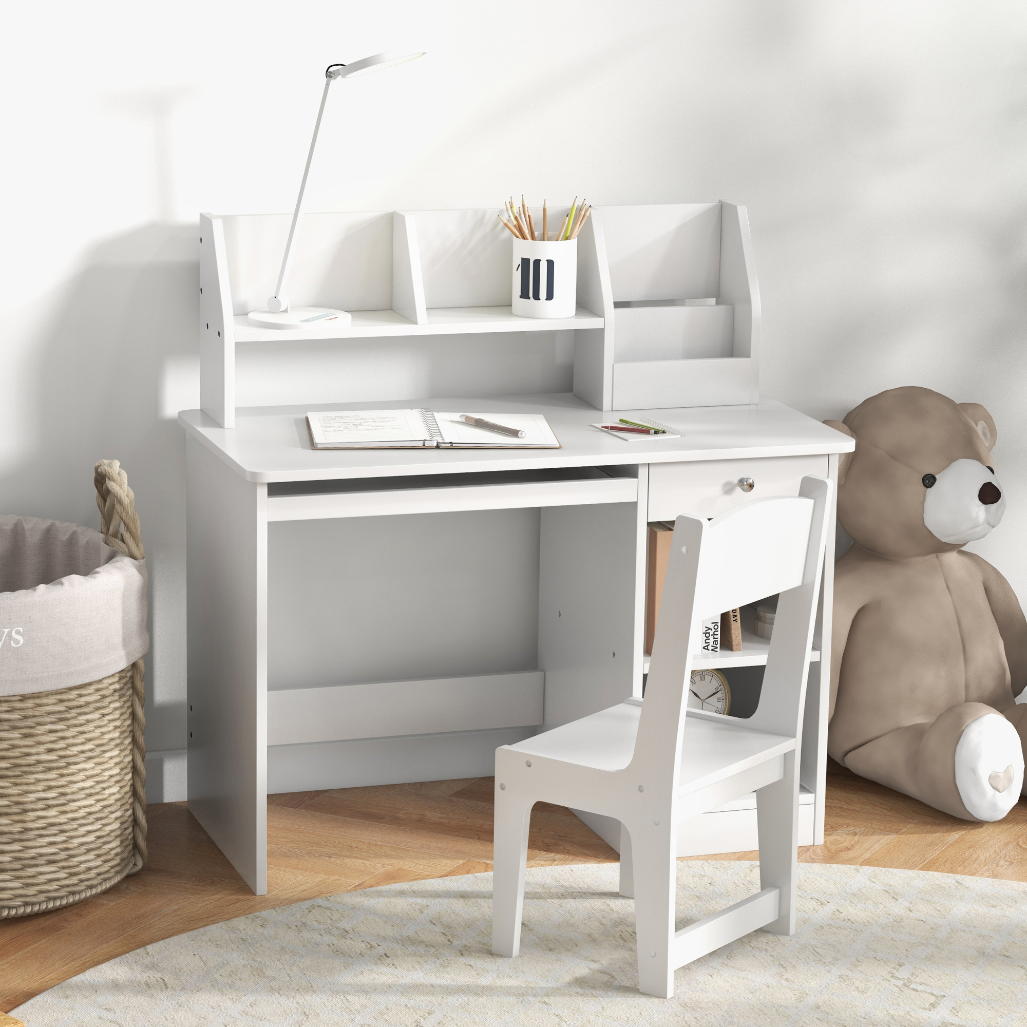 Una scrivania bianca per bambini con lampada, sedia, orsacchiotto e libri. Un cesto e un tappeto sono in primo piano.