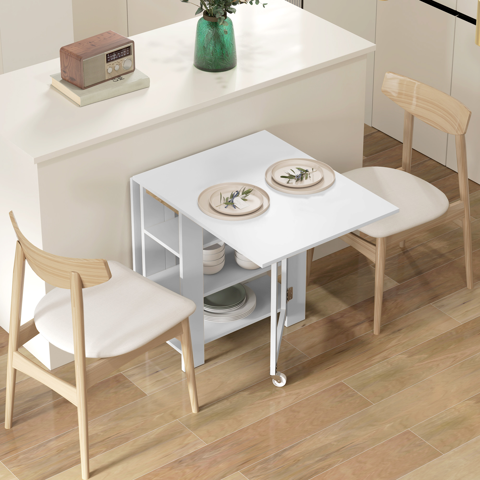 Un tavolo pieghevole bianco con due piatti apparecchiati. Due sedie sono disposte. Pavimento in legno e sfondo chiaro.