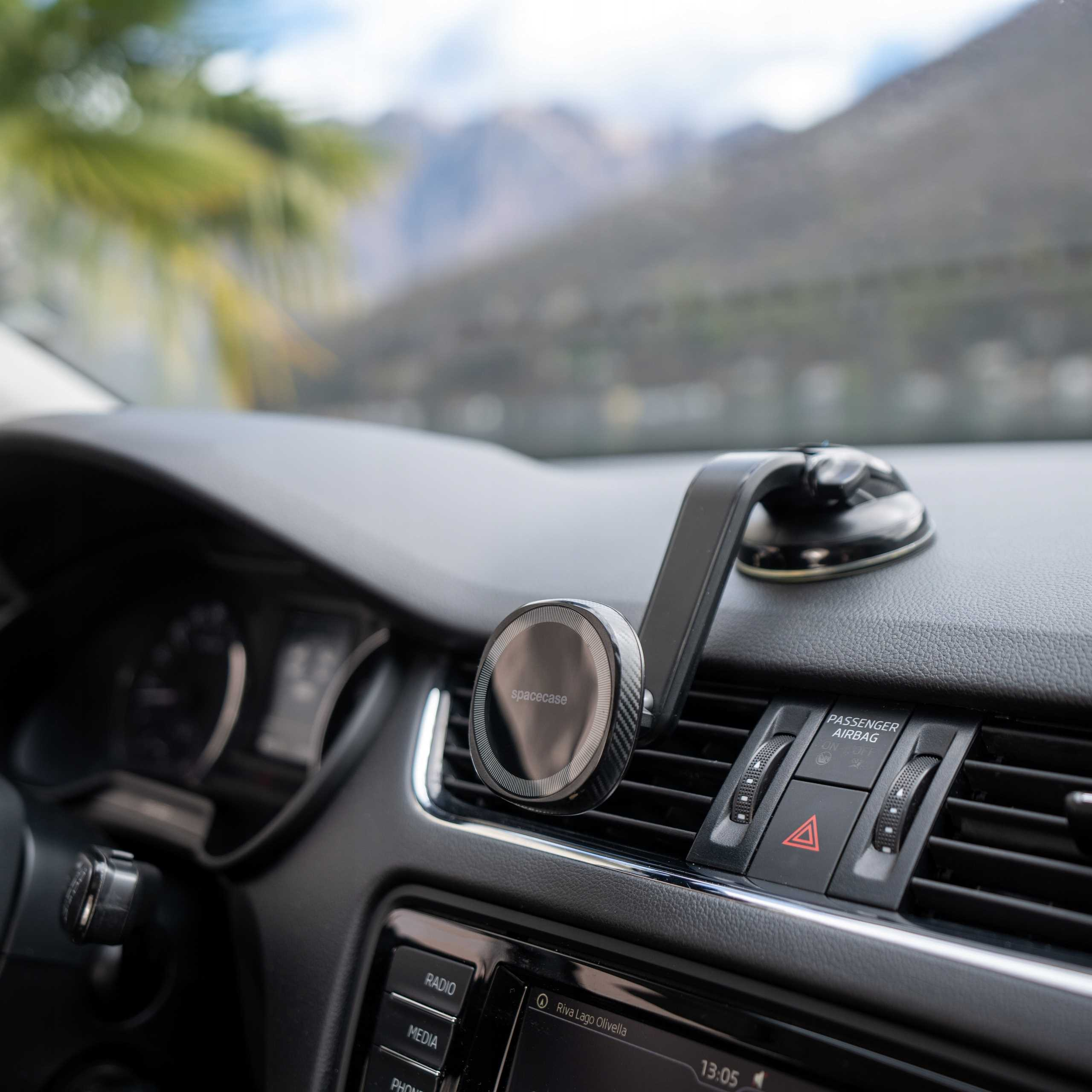Wnętrze samochodu z uchwytem na telefon i deską rozdzielczą. Tło przedstawia góry i palmy. Uchwyt ma markę 'spacecase'.