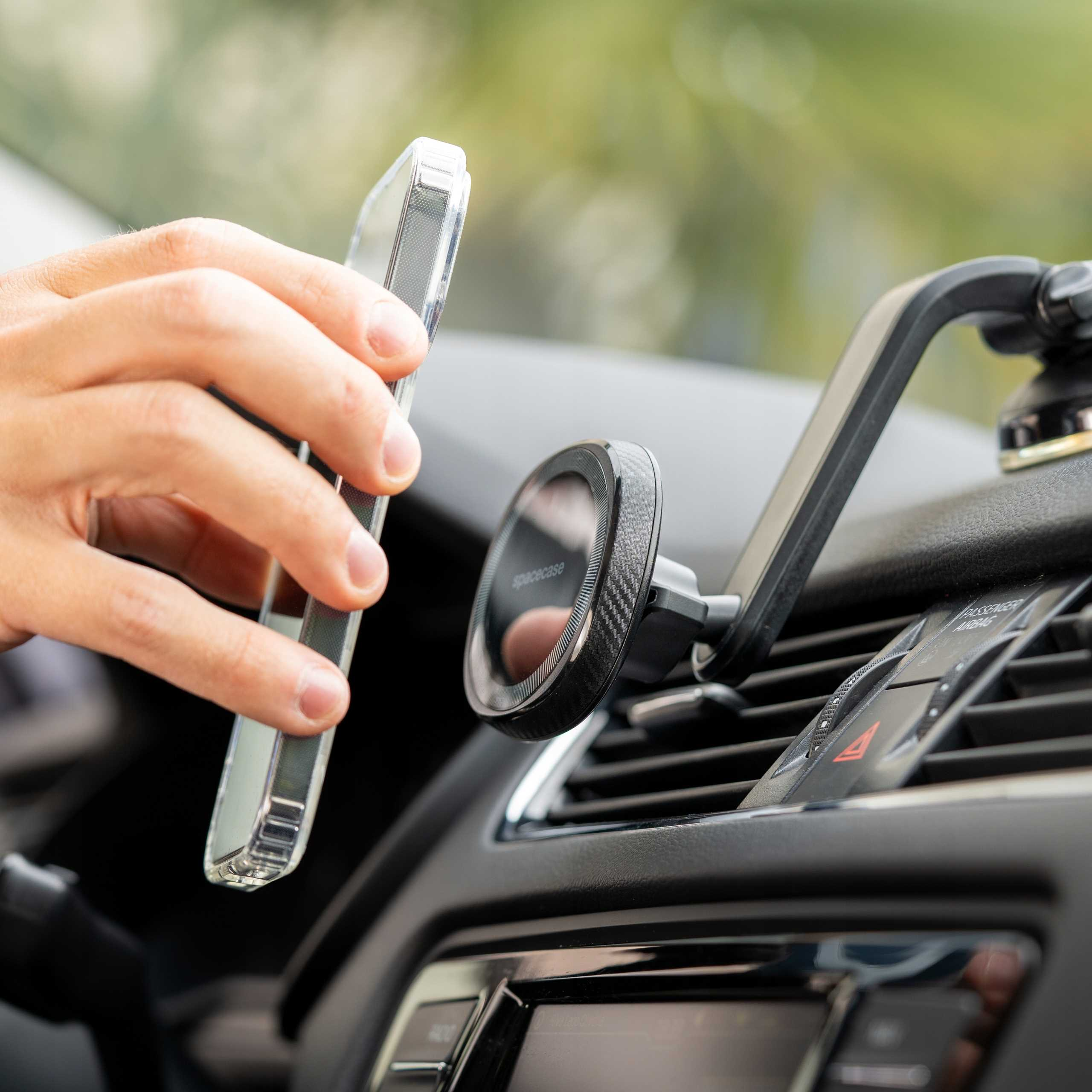 Ręka trzyma przezroczyste etui na telefon w pobliżu uchwytu samochodowego. Deska rozdzielcza jest w tle.