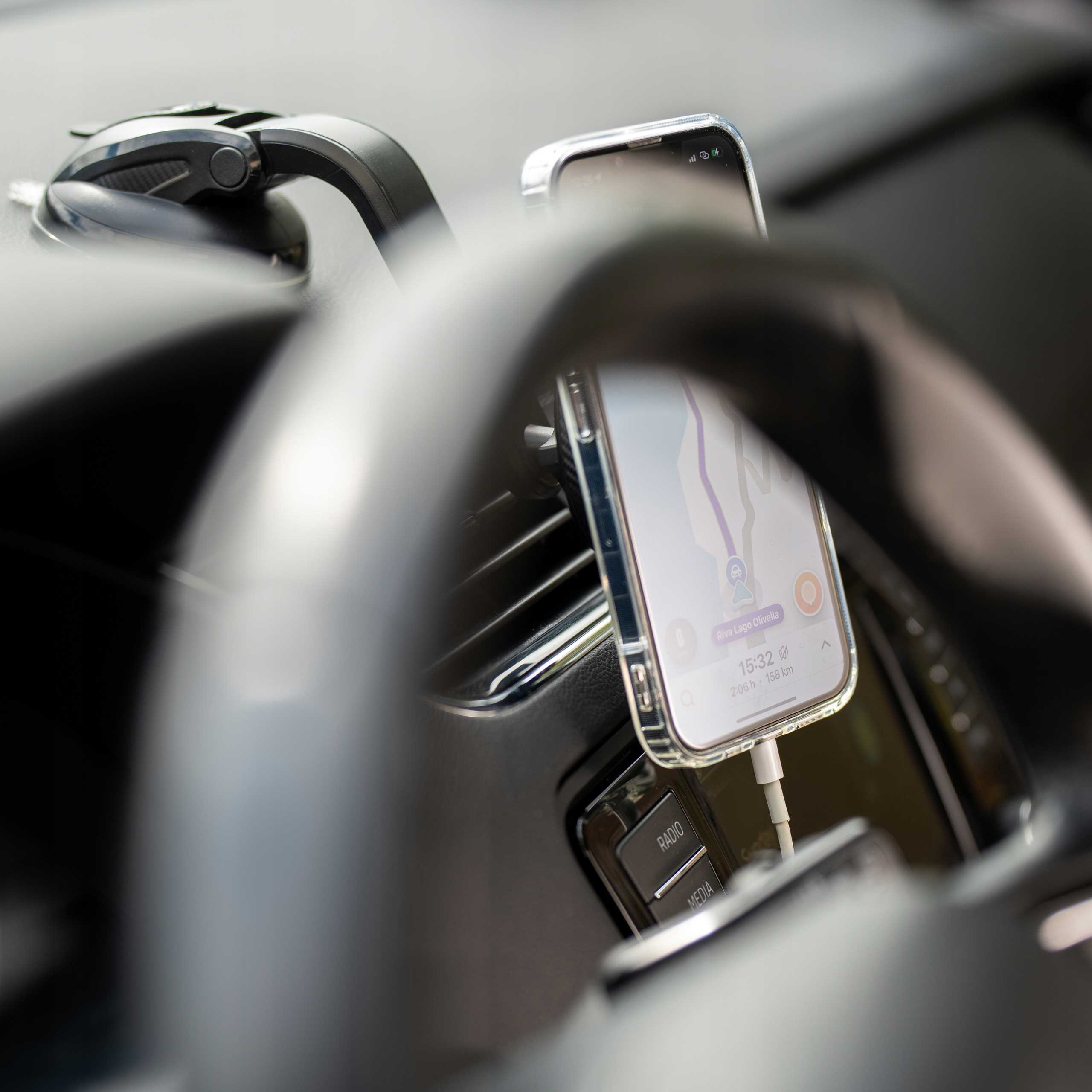 Telefon w uchwycie samochodowym, pokazujący aplikację nawigacyjną. Widoczna kierownica i deska rozdzielcza. Telefon się ładuje.