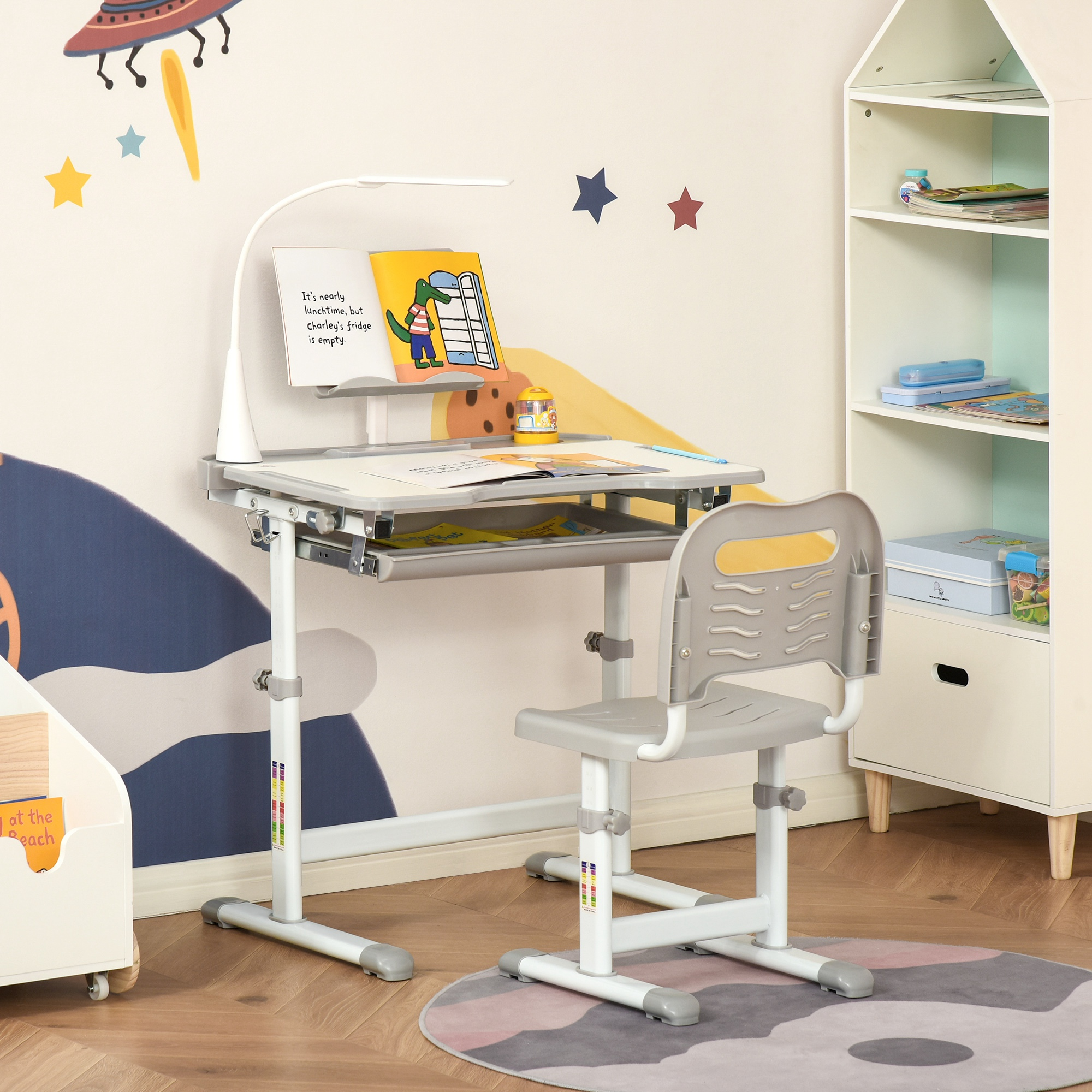Una scrivania per bambini con sedia, libri e lampada, in una stanza con decorazioni murali a tema stelle e spazio.