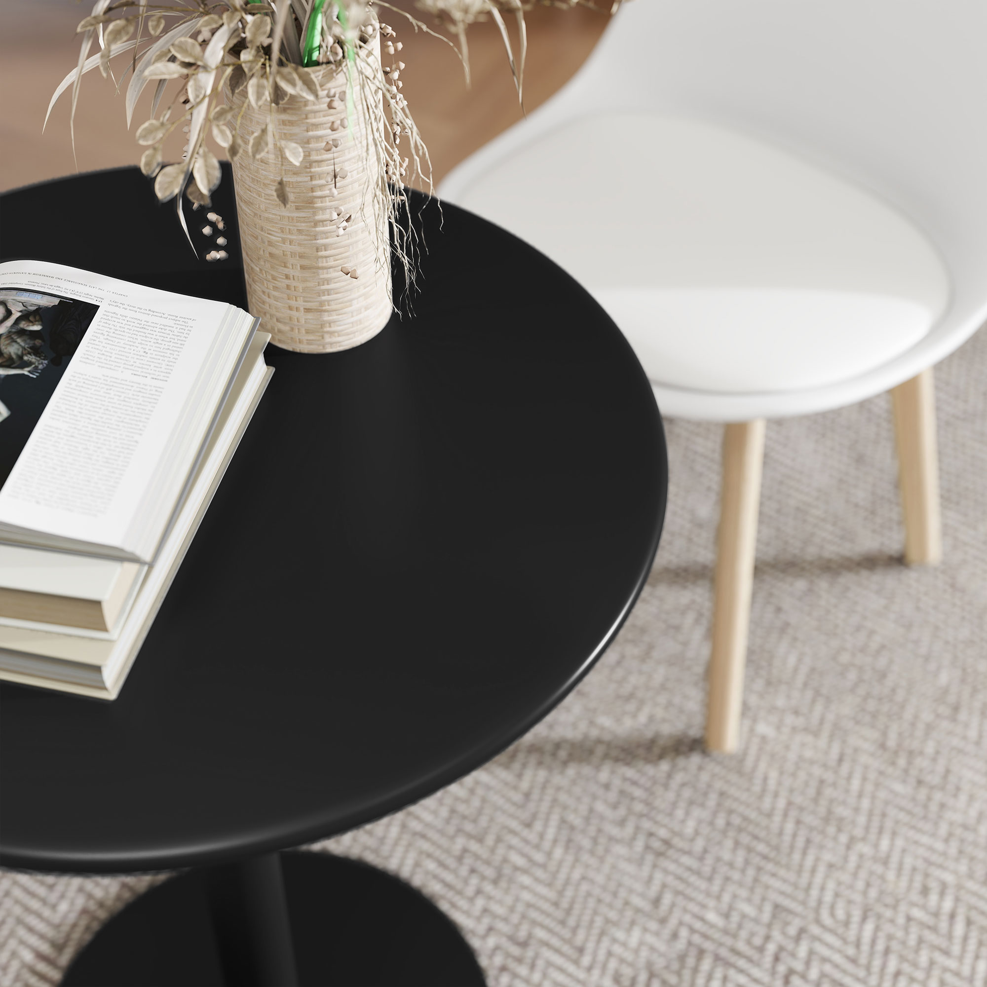 Un tavolo nero con libri e un vaso con fiori secchi. Una sedia bianca è accanto su un tappeto fantasia.