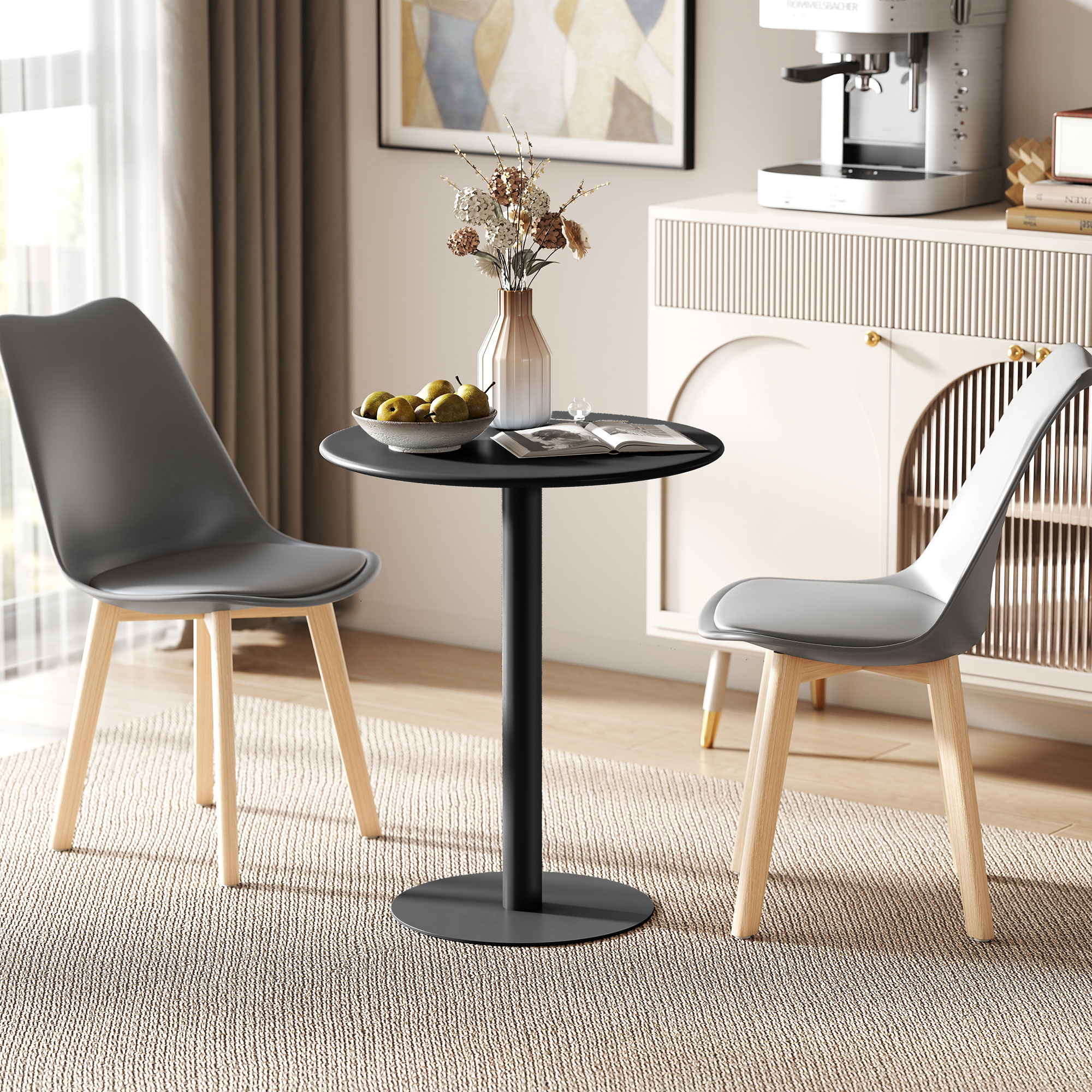 Un tavolo rotondo nero con pere, due sedie grigie con gambe in legno. Sullo sfondo una credenza con una macchina per il caffè.