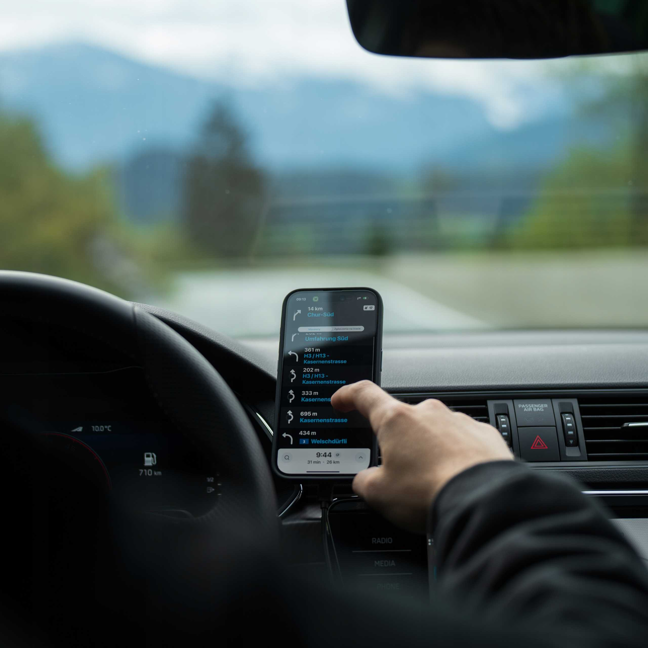 Osoba używa telefonu z nawigacją w samochodzie. Góry widoczne przez przednią szybę.