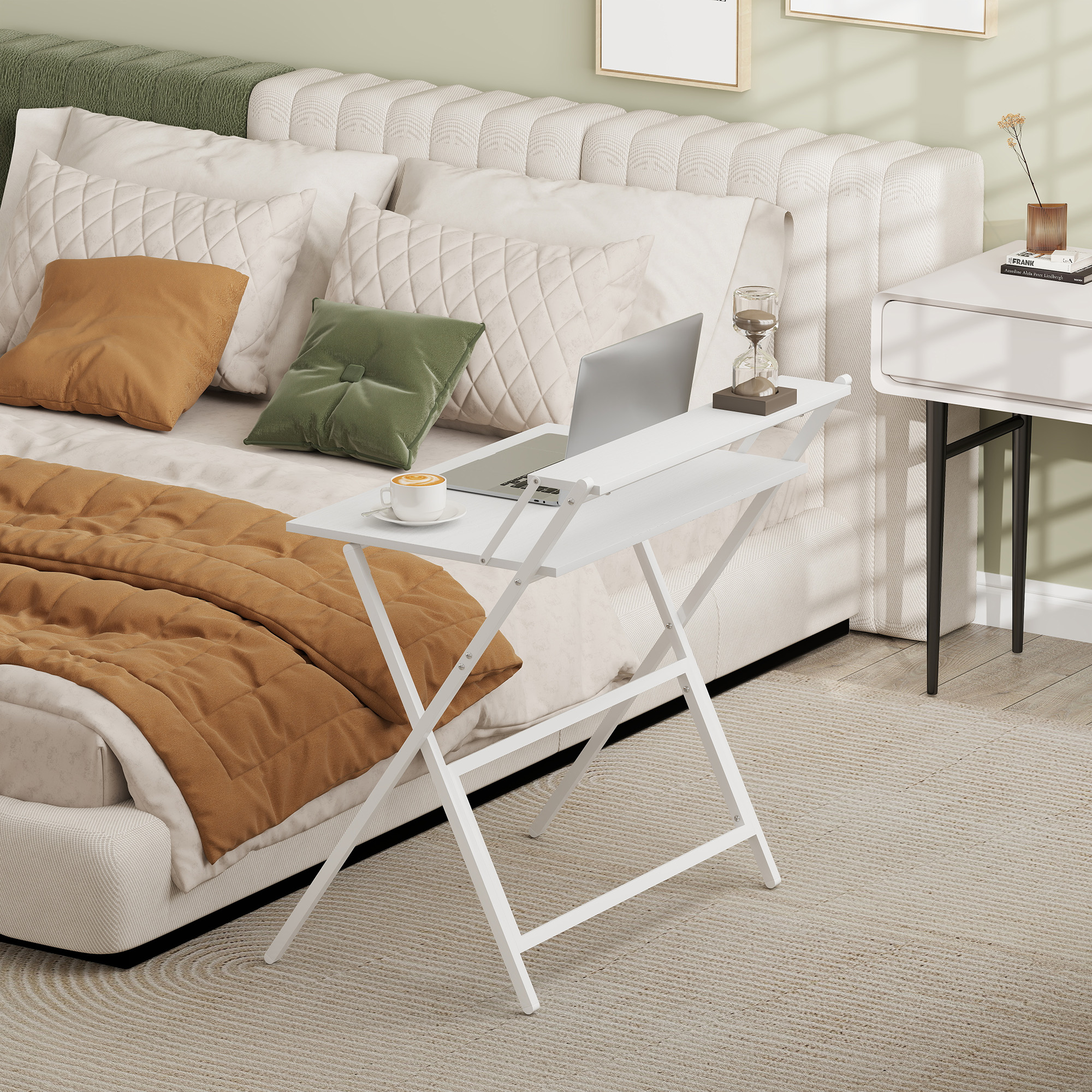 Un tavolo bianco per laptop con tazza di caffè e laptop sopra. Letto con cuscini e coperta. Comodino con decorazioni.