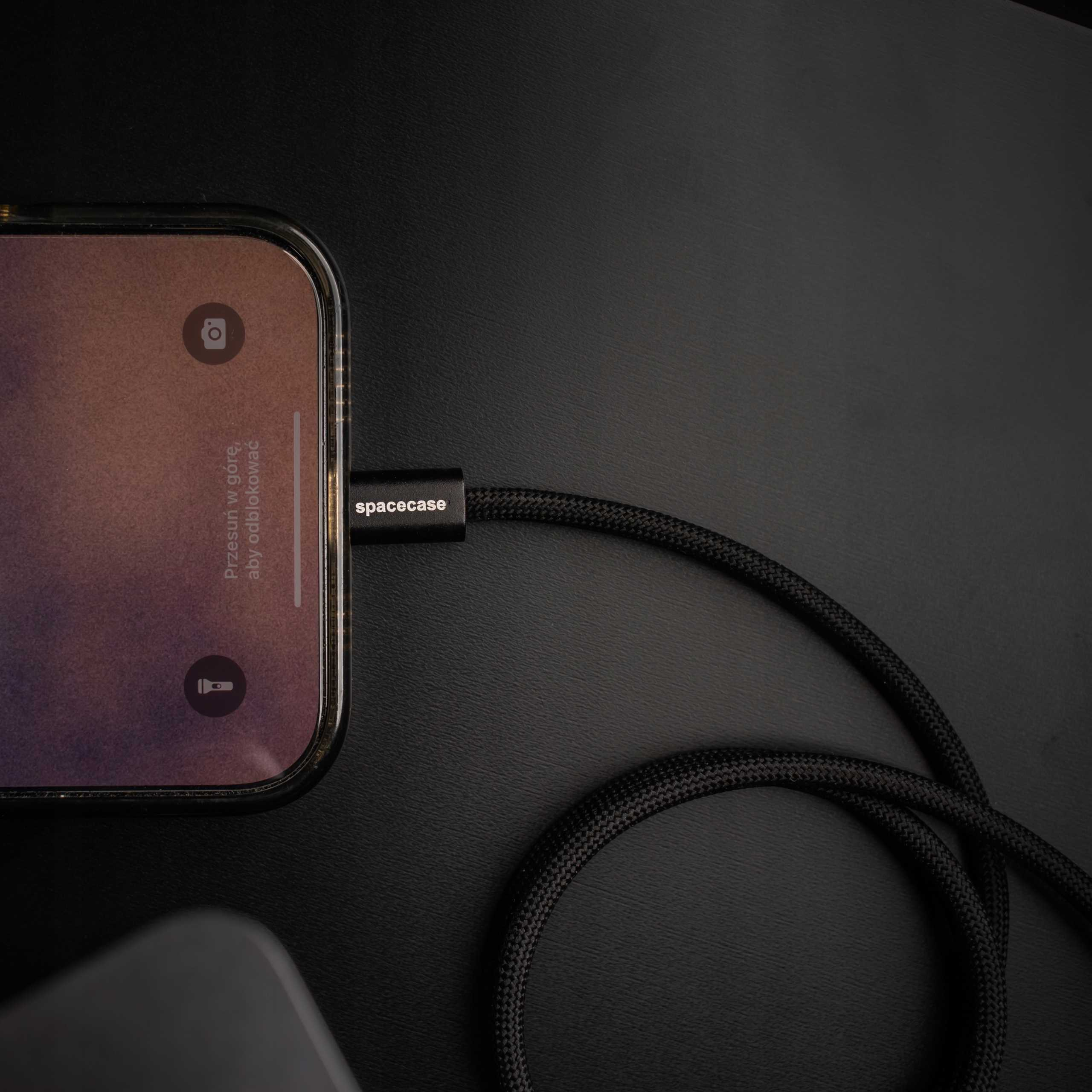 iPhone z podłączonym czarnym plecionym kablem ładującym. Telefon wyświetla ekran blokady z ikoną aparatu.