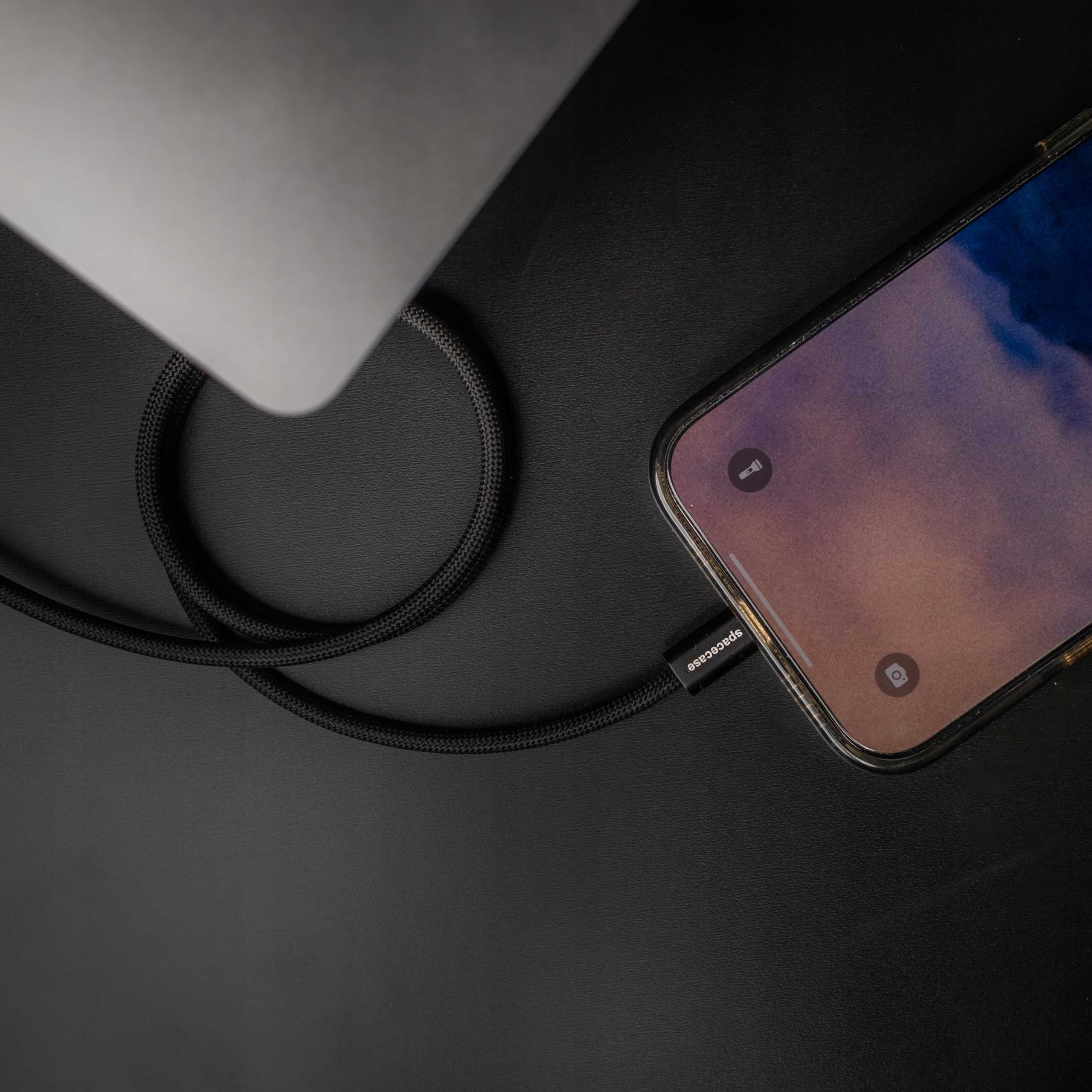 Telefon jest połączony z laptopem czarnym kablem. Ekran telefonu pokazuje zachmurzone niebo.