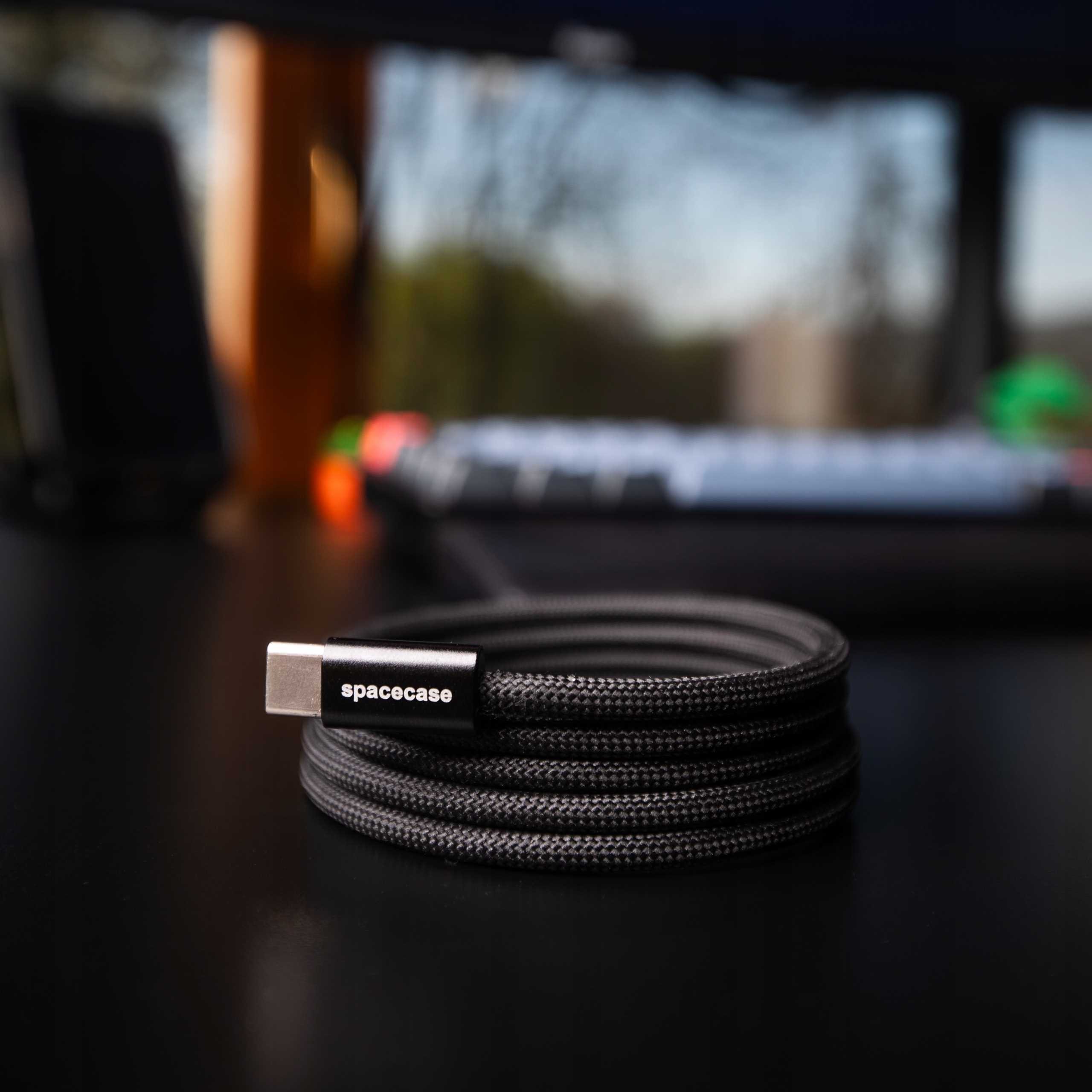 Czarny kabel USB-C zwinięty na czarnej powierzchni. Na złączu napis 'spacecase'. W tle klawiatura.