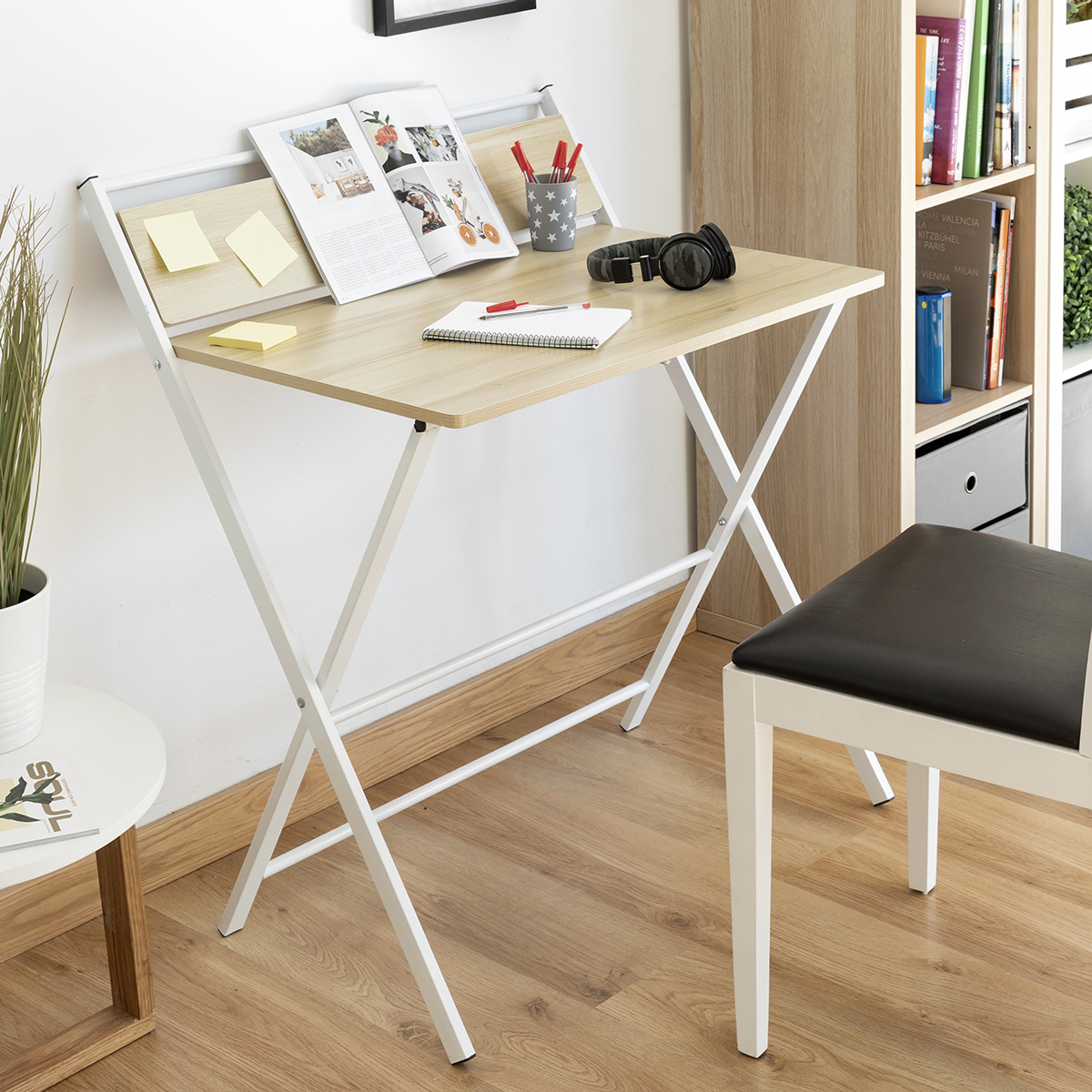 Un escritorio de madera clara con patas blancas. Sobre el escritorio hay una revista, bolígrafos, auriculares y un bloc de notas. Una silla está cerca.