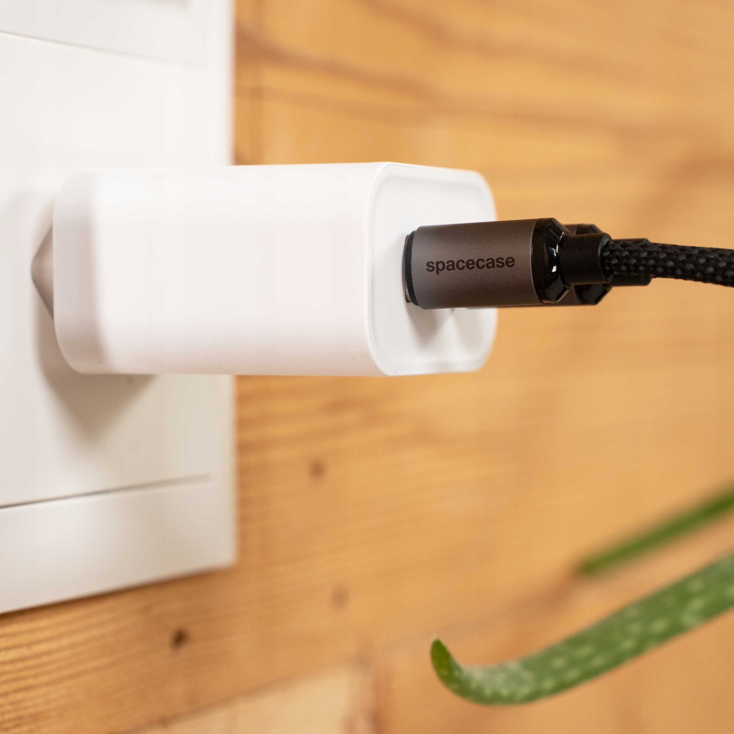 Biała ładowarka jest podłączona do ściany. Czarny kabel ze słowem spacecase jest podłączony.