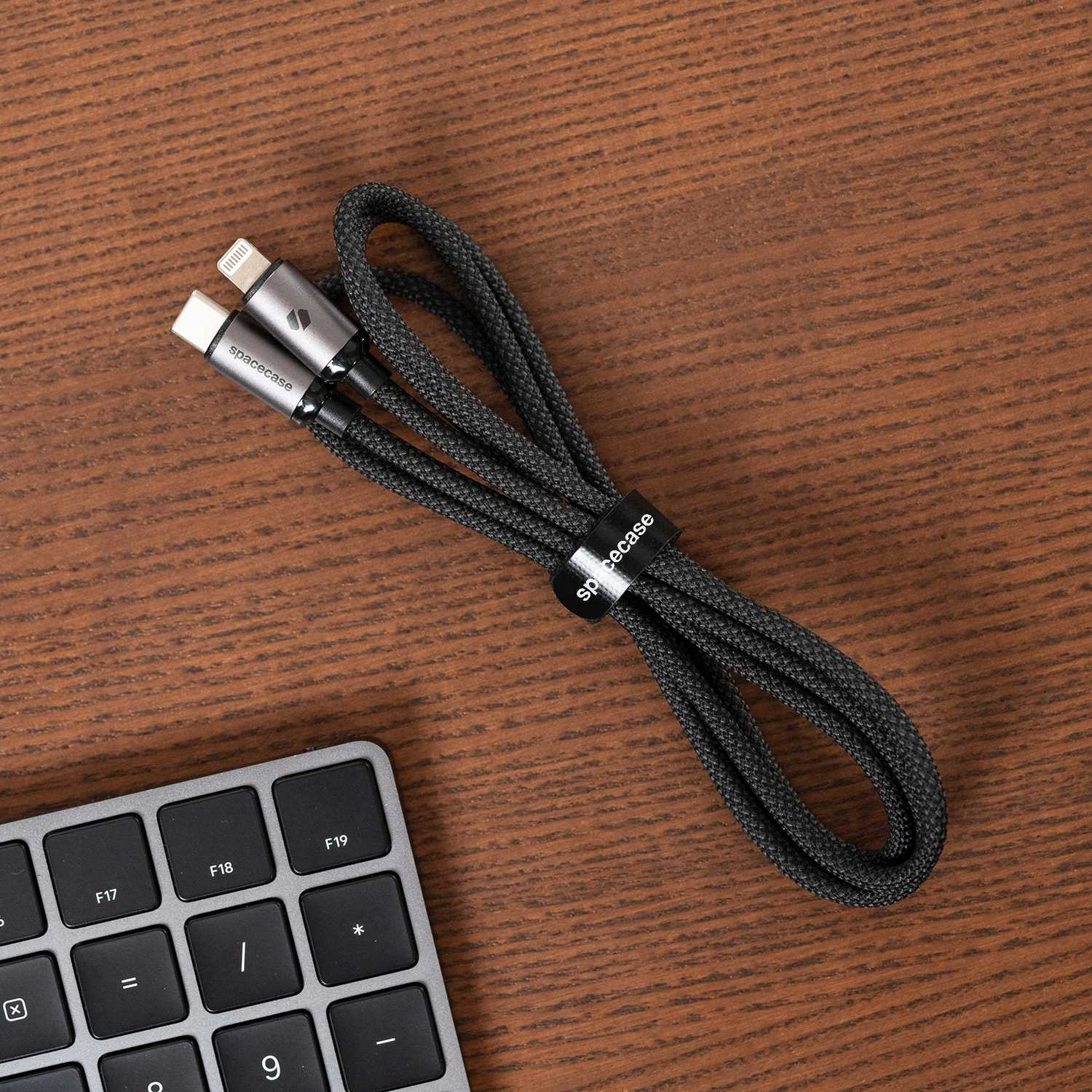 Czarny pleciony kabel USB-C do Lightning z logo Spacecase na drewnianym biurku. Klawiatura w rogu.