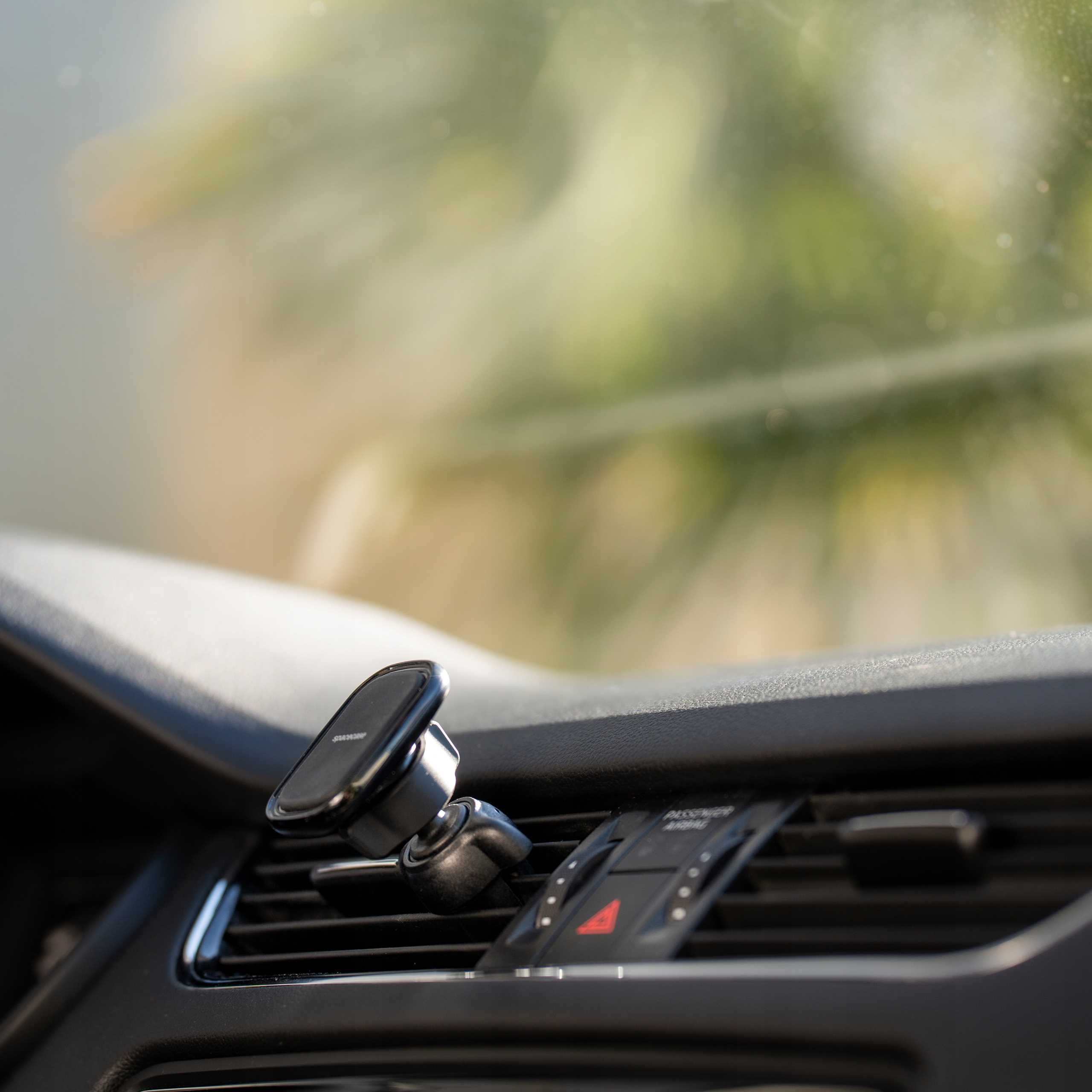 Wnętrze samochodu z uchwytem na telefon i szczegółami deski rozdzielczej. Rozmyte zielone i białe tło z zewnątrz.